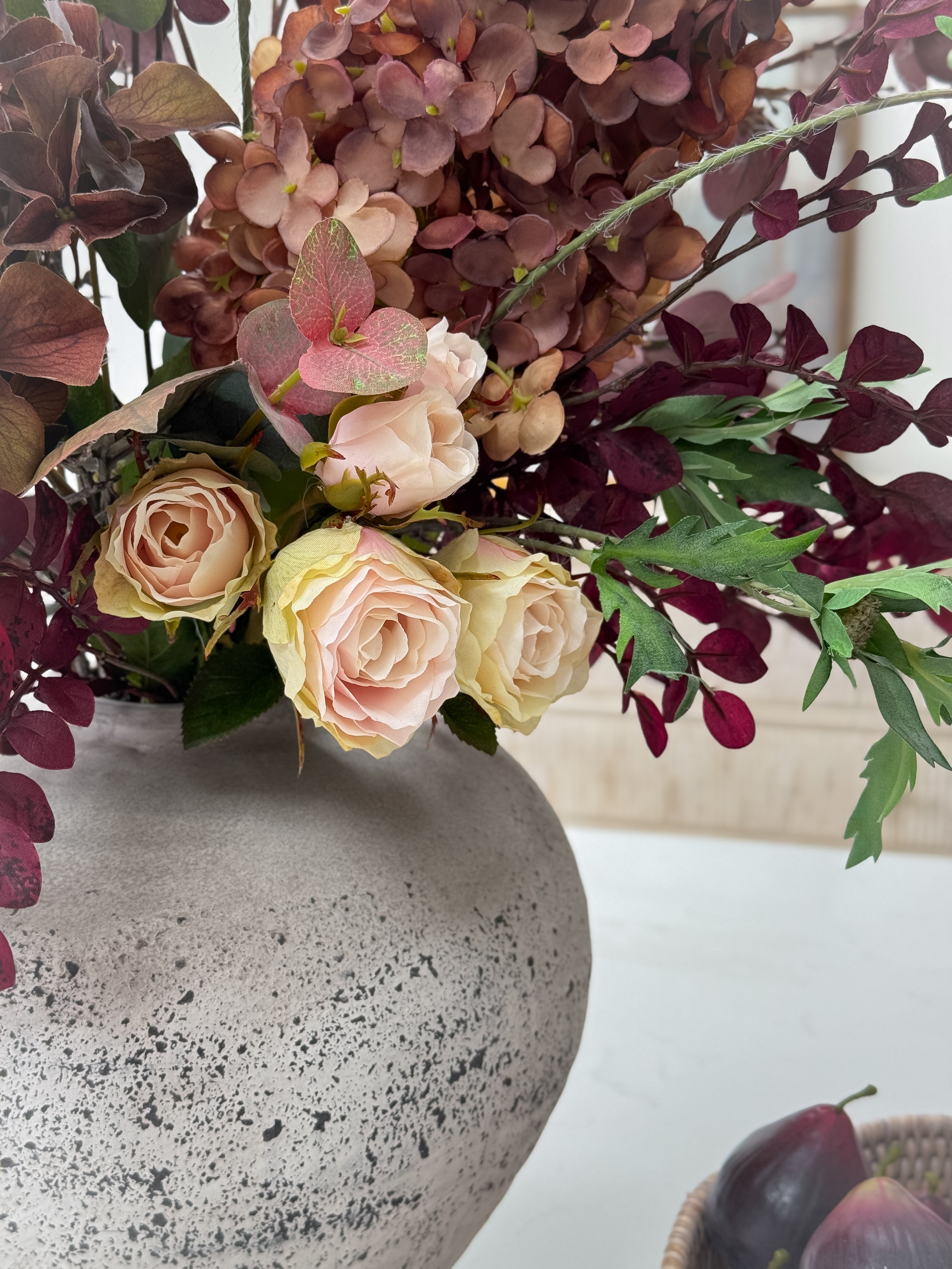 Decorative autumn floral arrangement in a textured vase on a white surface.