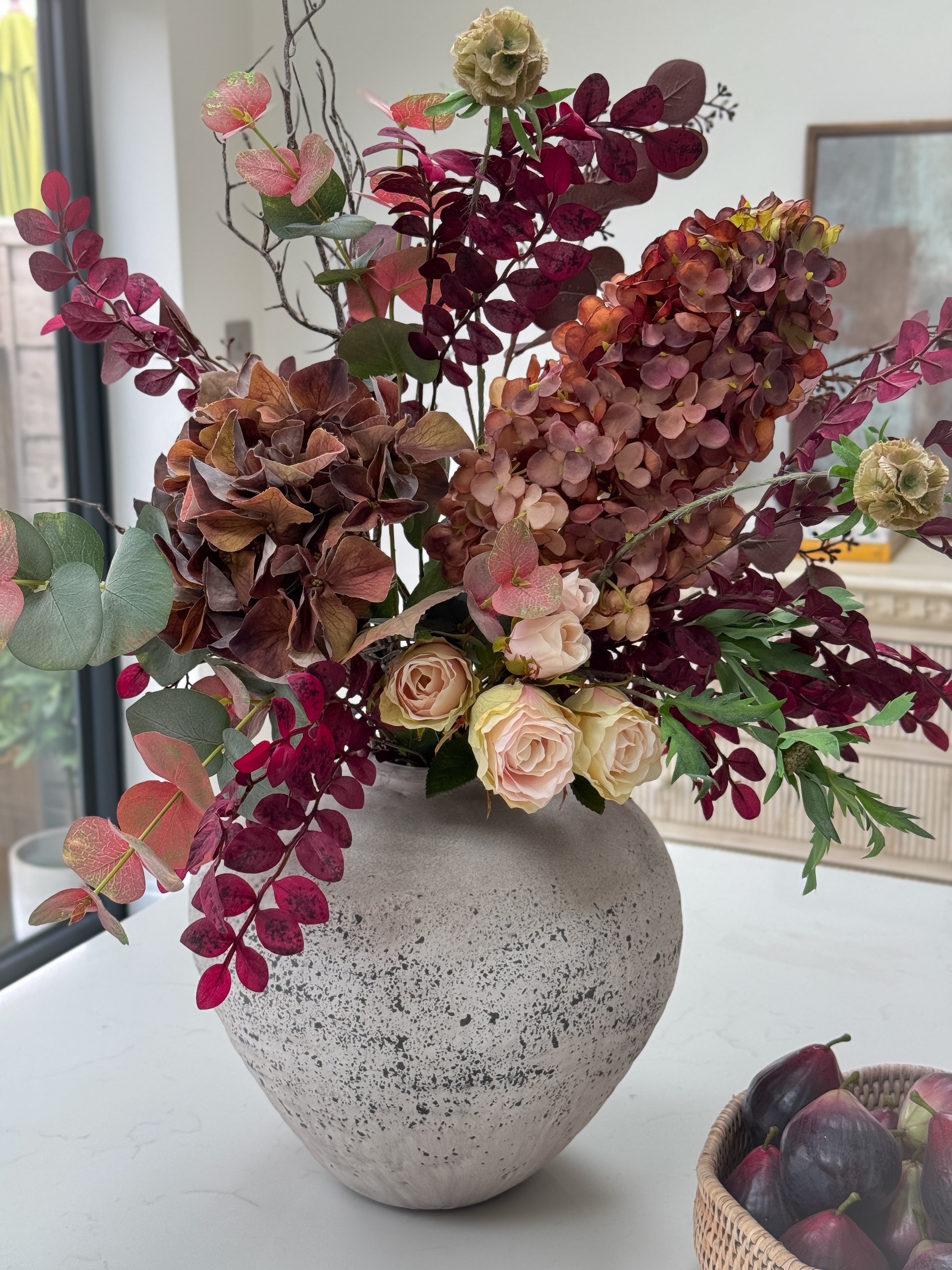Decorative faux autumn floral arrangement in a textured vase on a table.