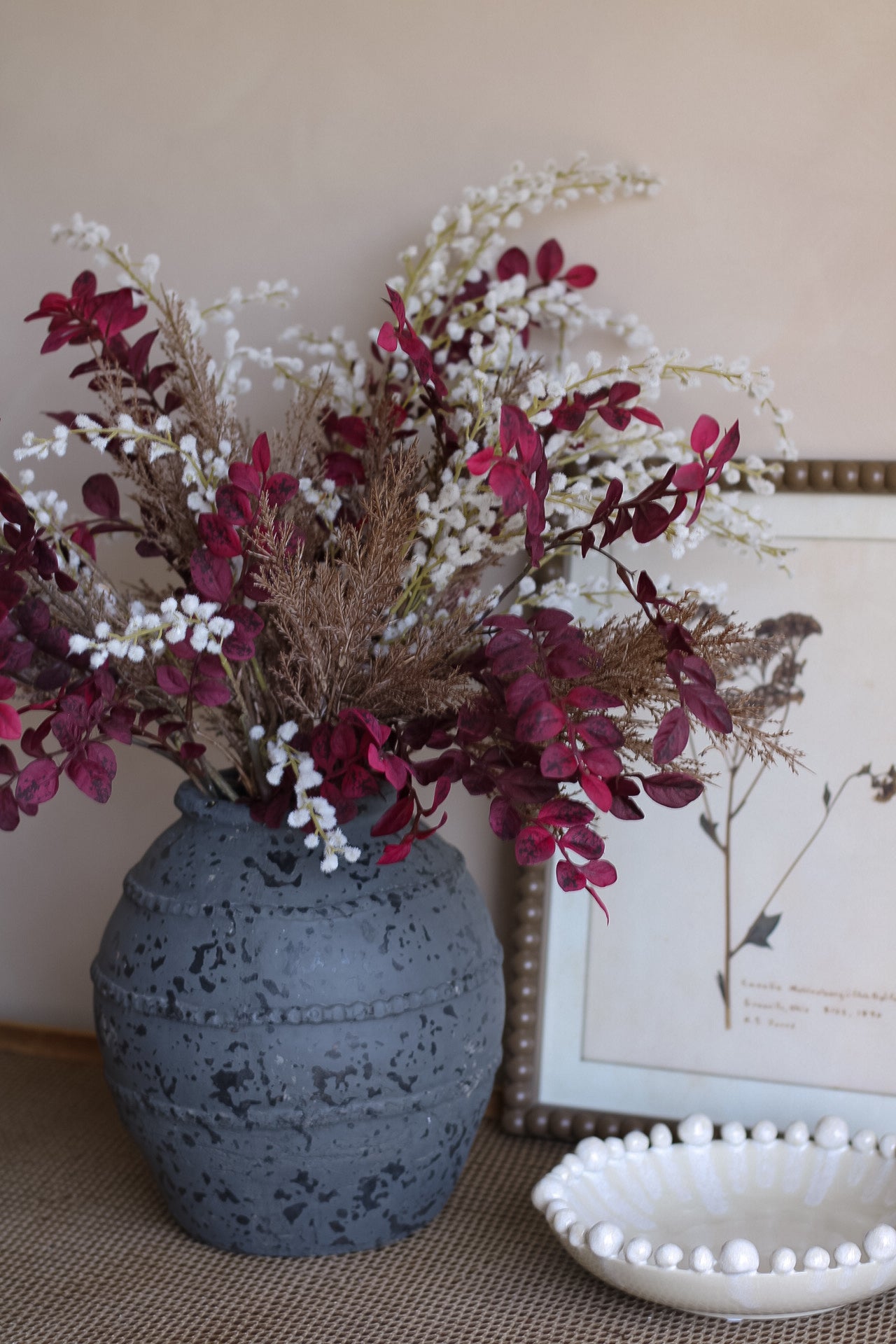 Decorative vase with autumn flowers on a table next to a framed picture