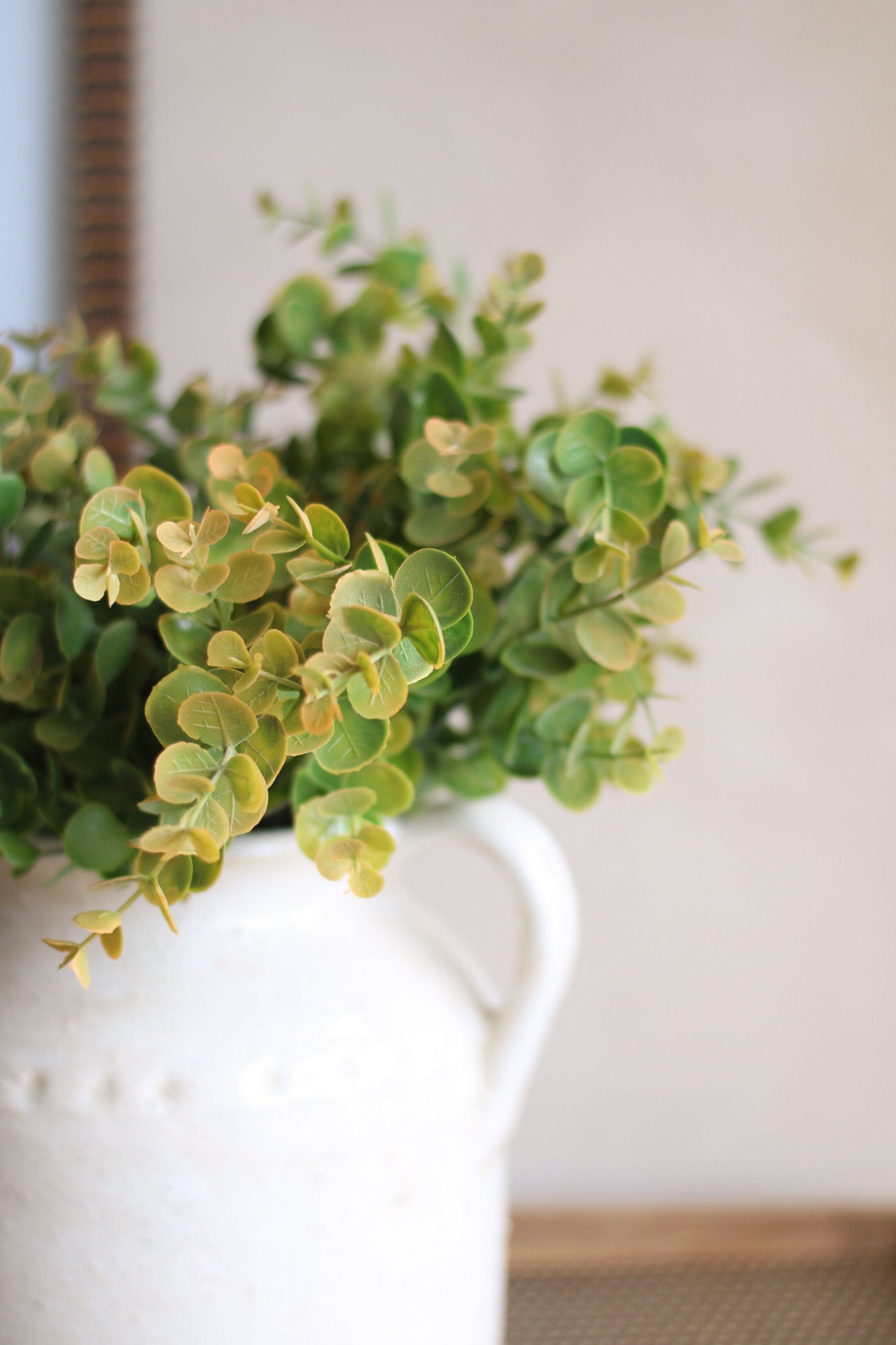 Green leaves in a white vase against a neutral background