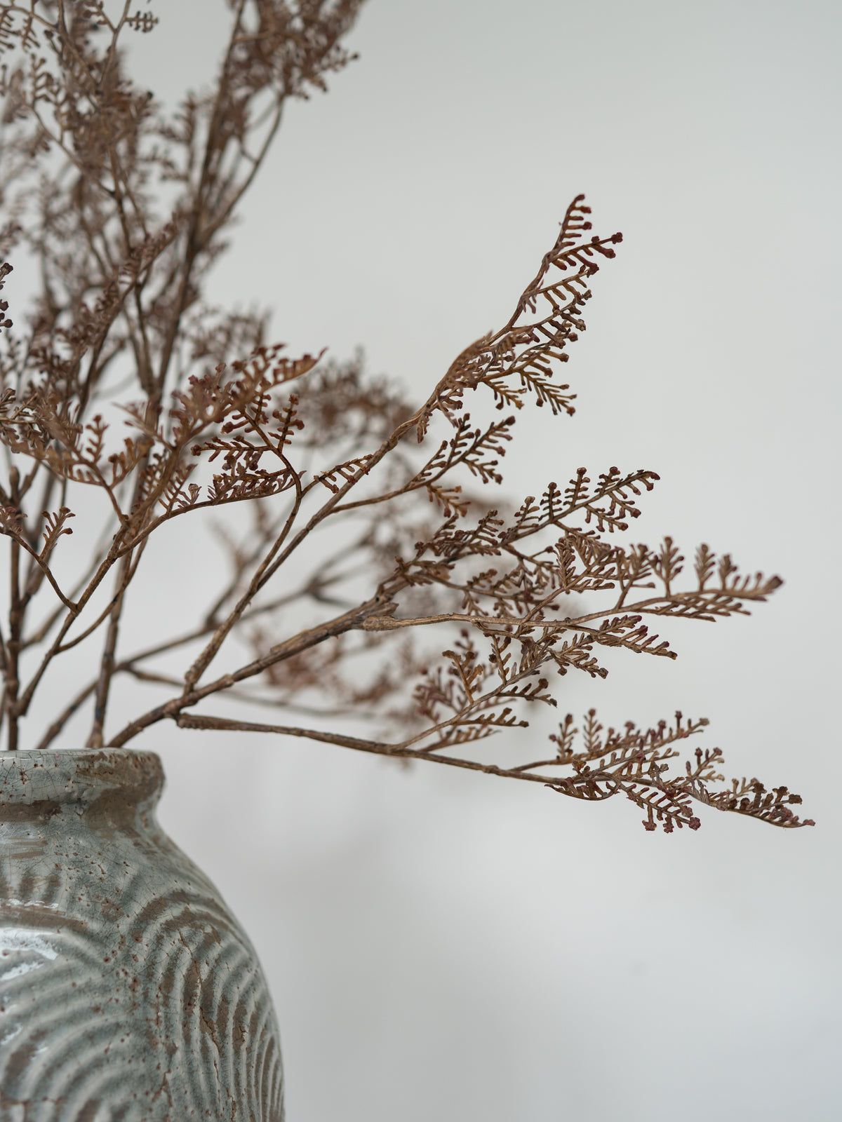 Dried brown botanical branches arranged in a textured gray ceramic vase against a soft light gray background.