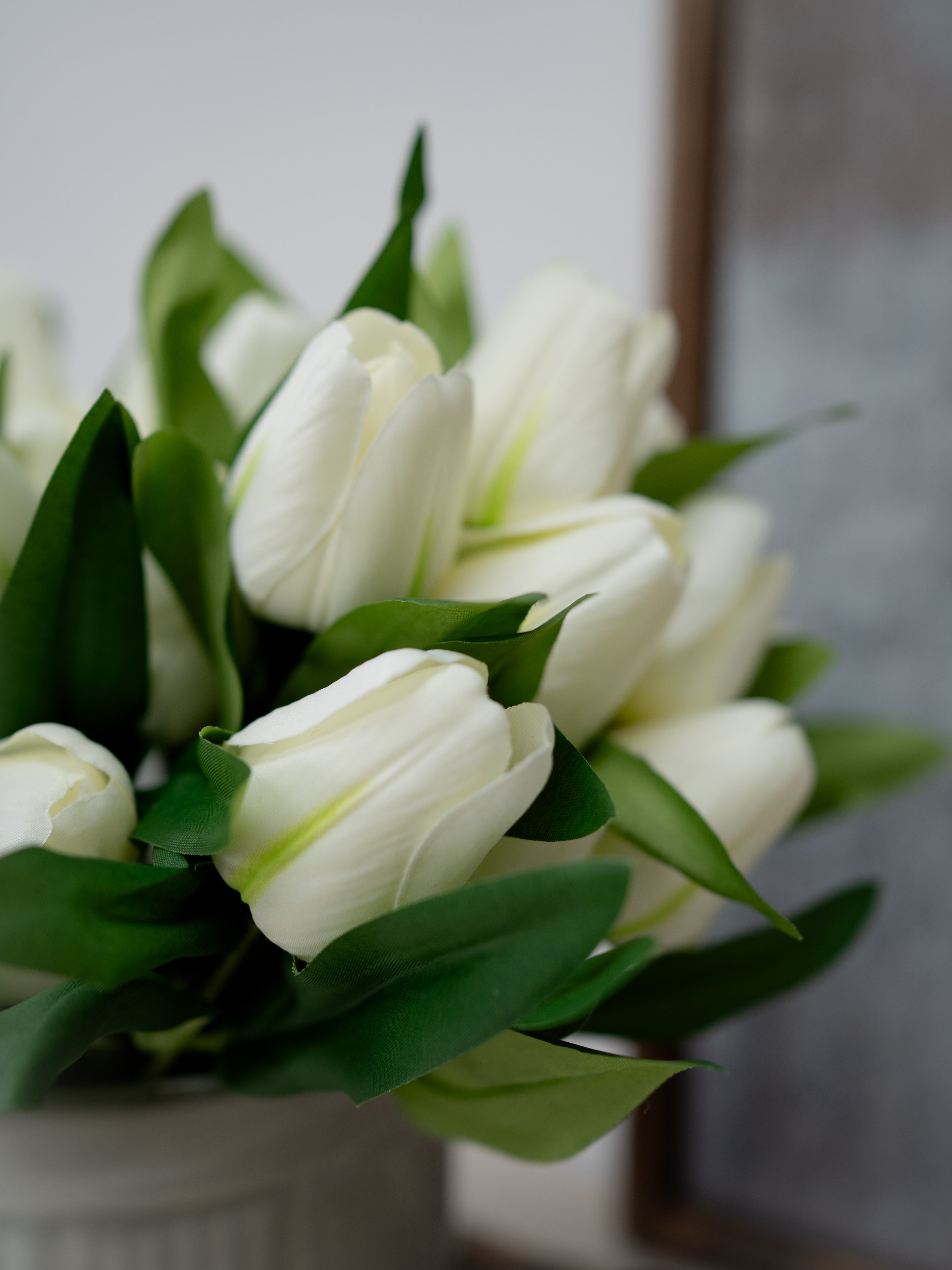 Bouquet of white tulips with green leaves in a white vase against a neutral background