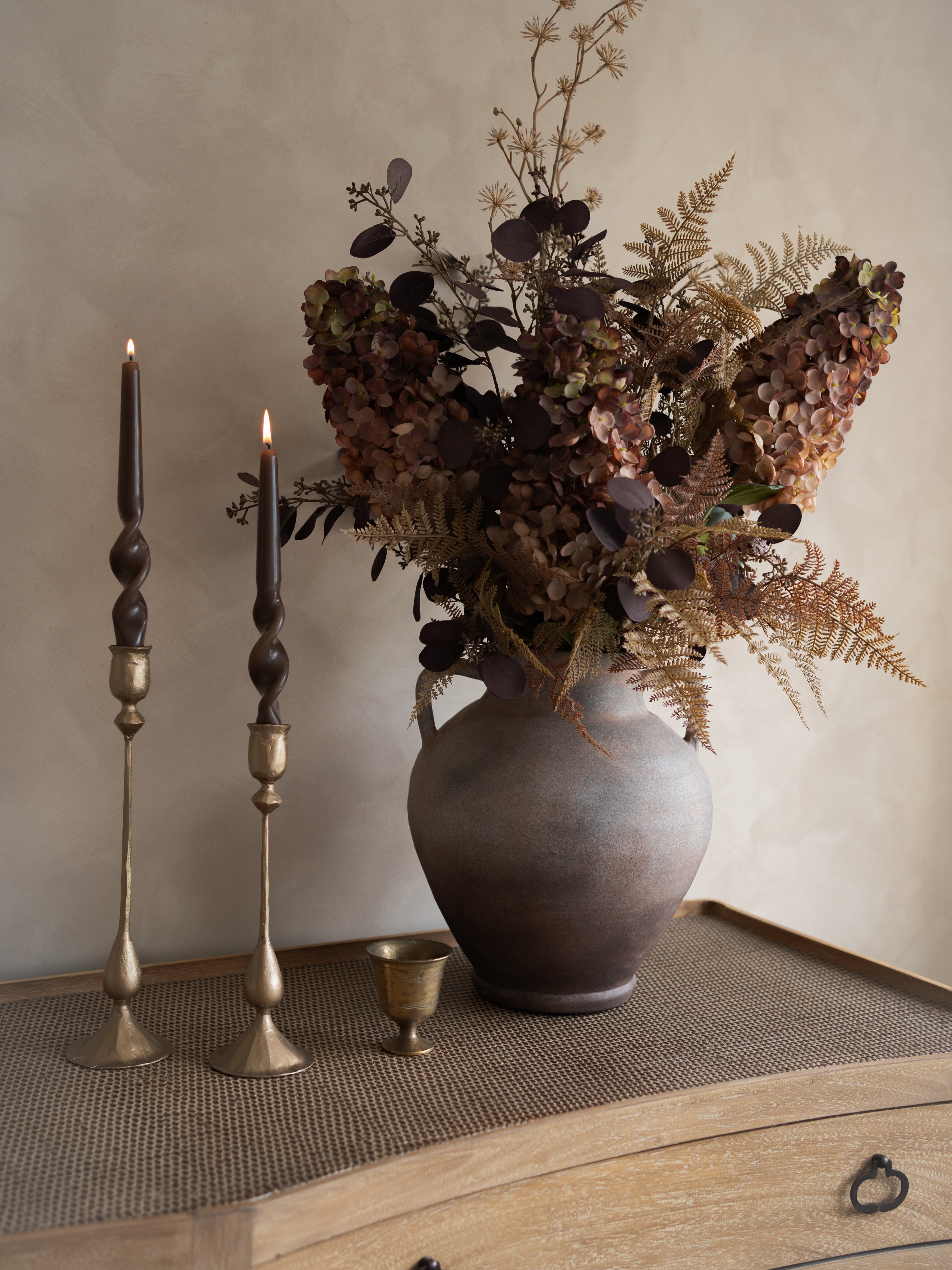 Decorative vase with faux autumn inspired floral arrangement and candles on a wooden surface