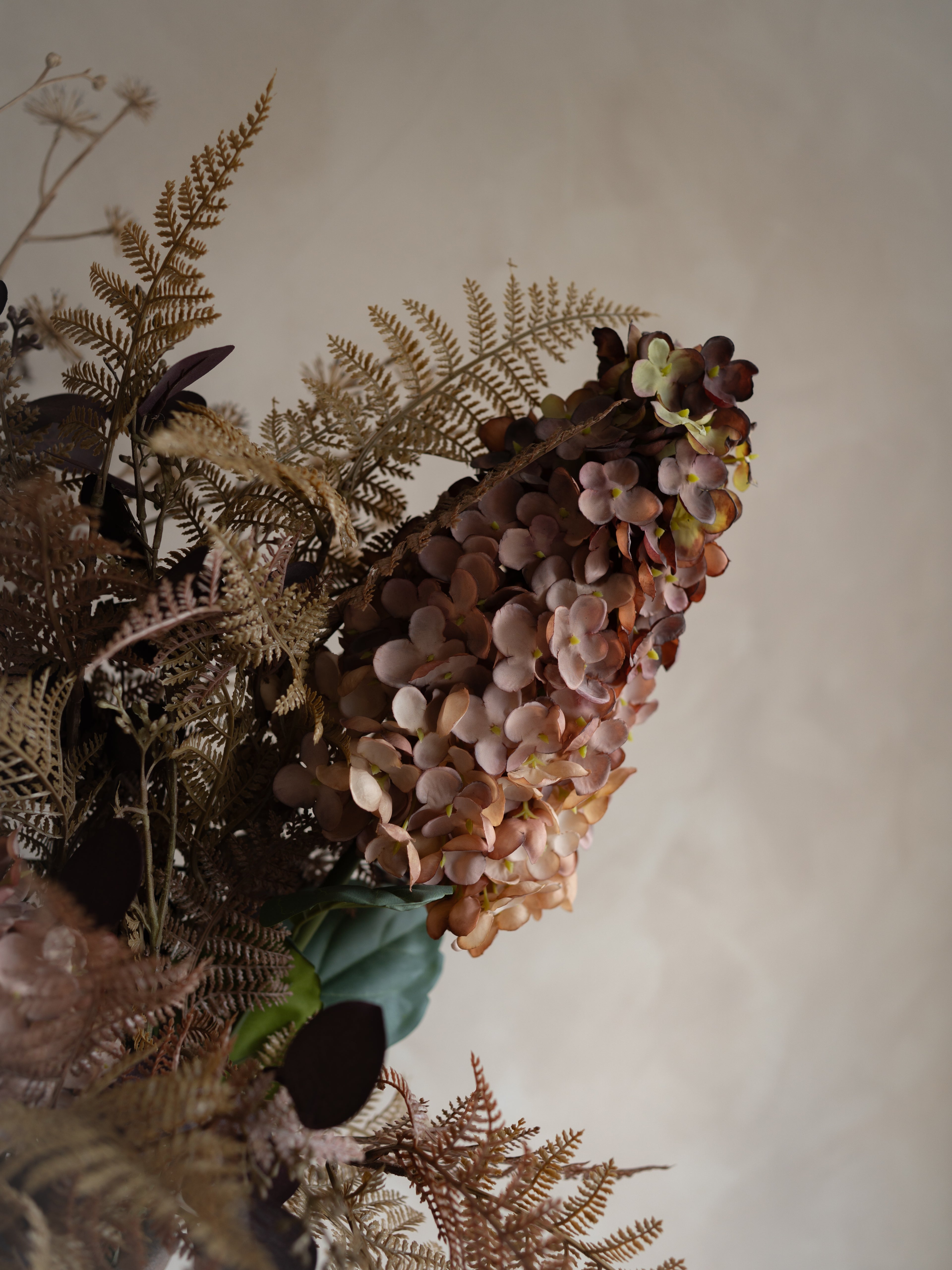 Bouquet of faux autumn flowers and herbs on a neutral background
