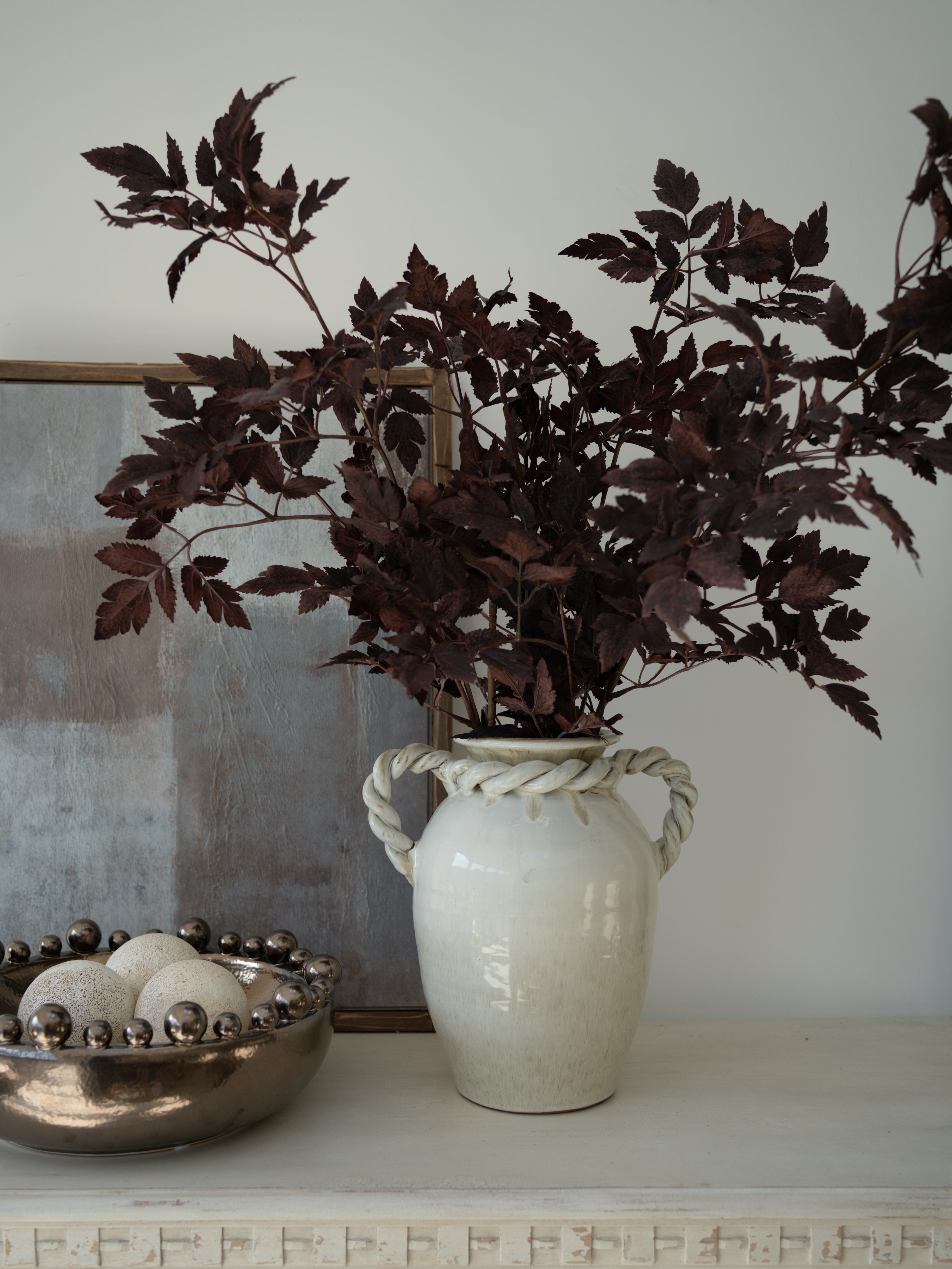 White vase with Faux Burgundy Physocarpus Diablo on a surface with a neutral background