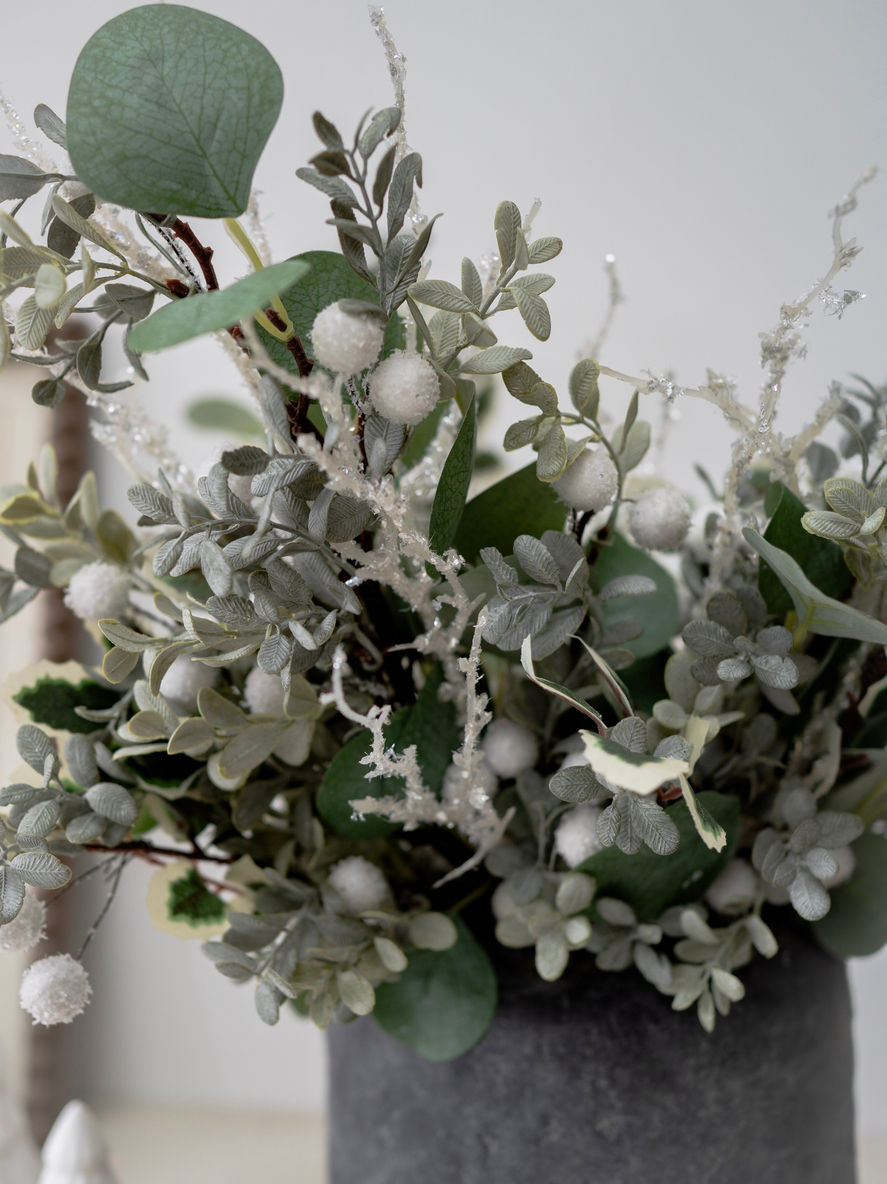 Decorative arrangement of faux christmas greenery and white berries in a gray vase against a neutral background