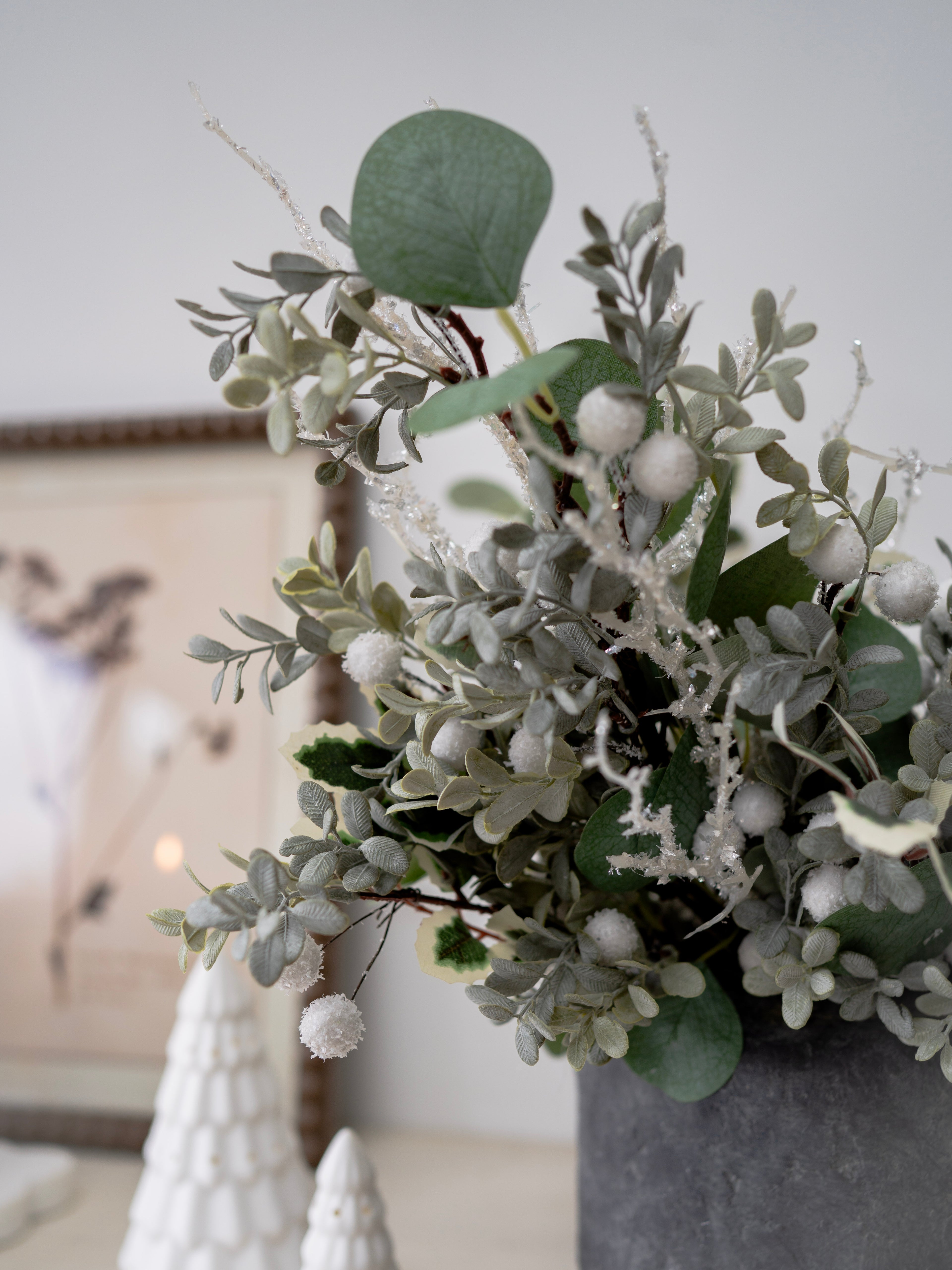 Decorative arrangement of faux christmas greenery and white berries in a vase on a neutral background