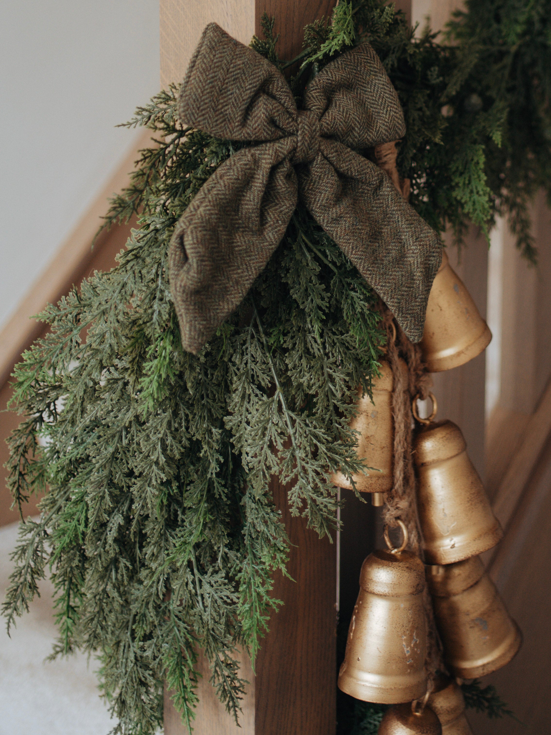 Decorative faux cypress garland with gold bells and a brown bow on a wooden surface.