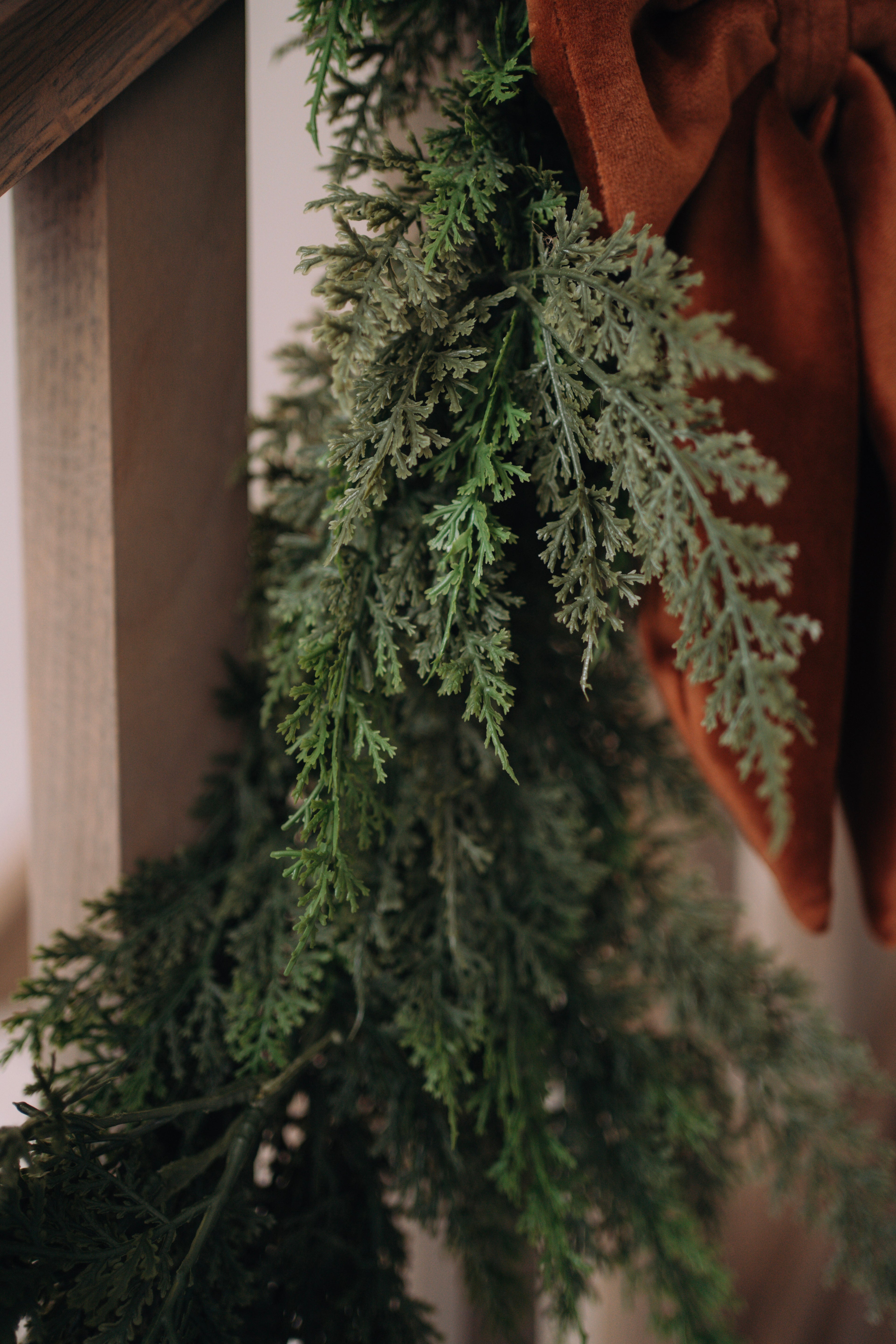 Up close of faux cypress garland with a brown fabric bow on a neutral background
