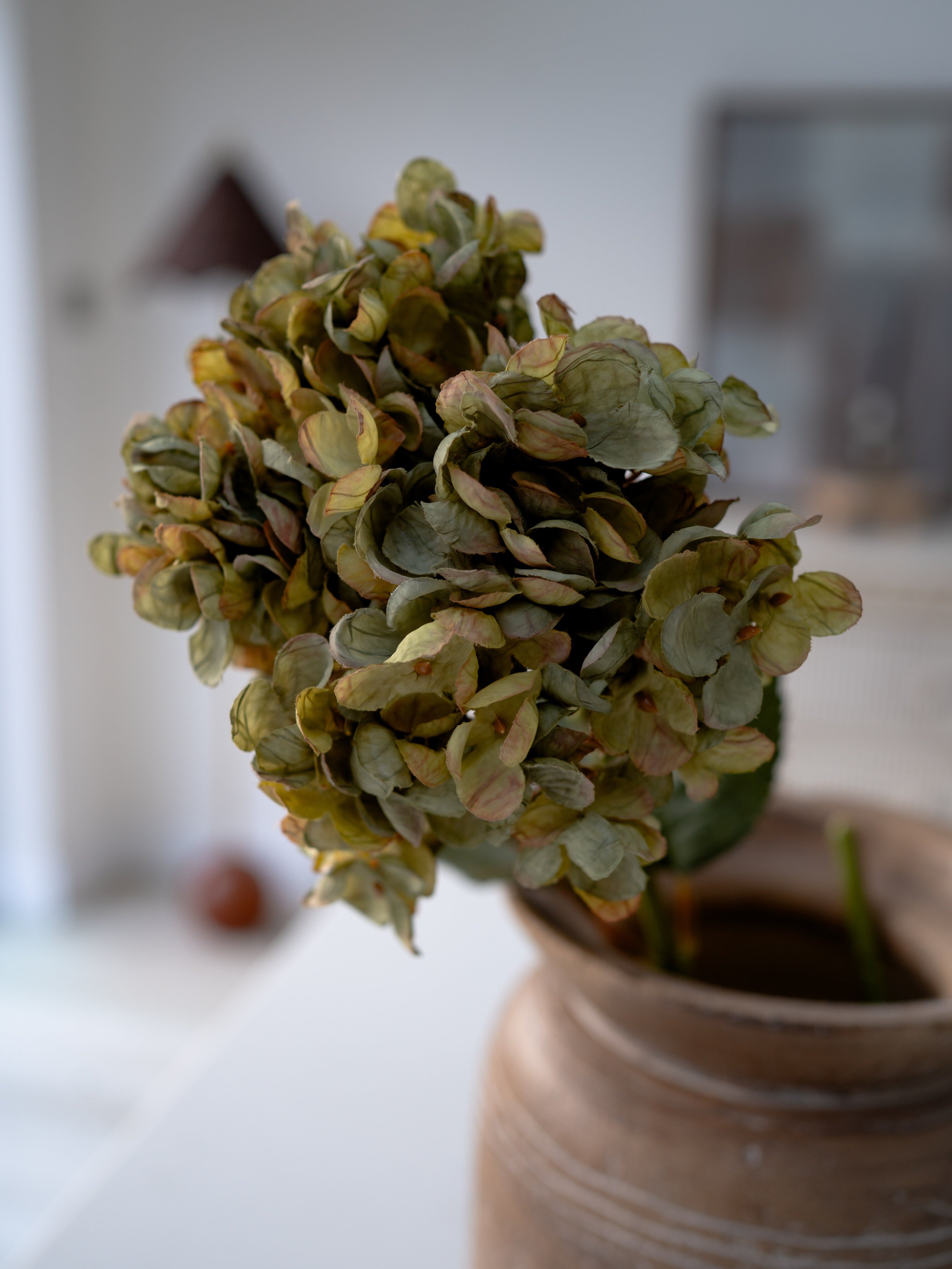 faux green flowers in a vase with a blurred indoor background
