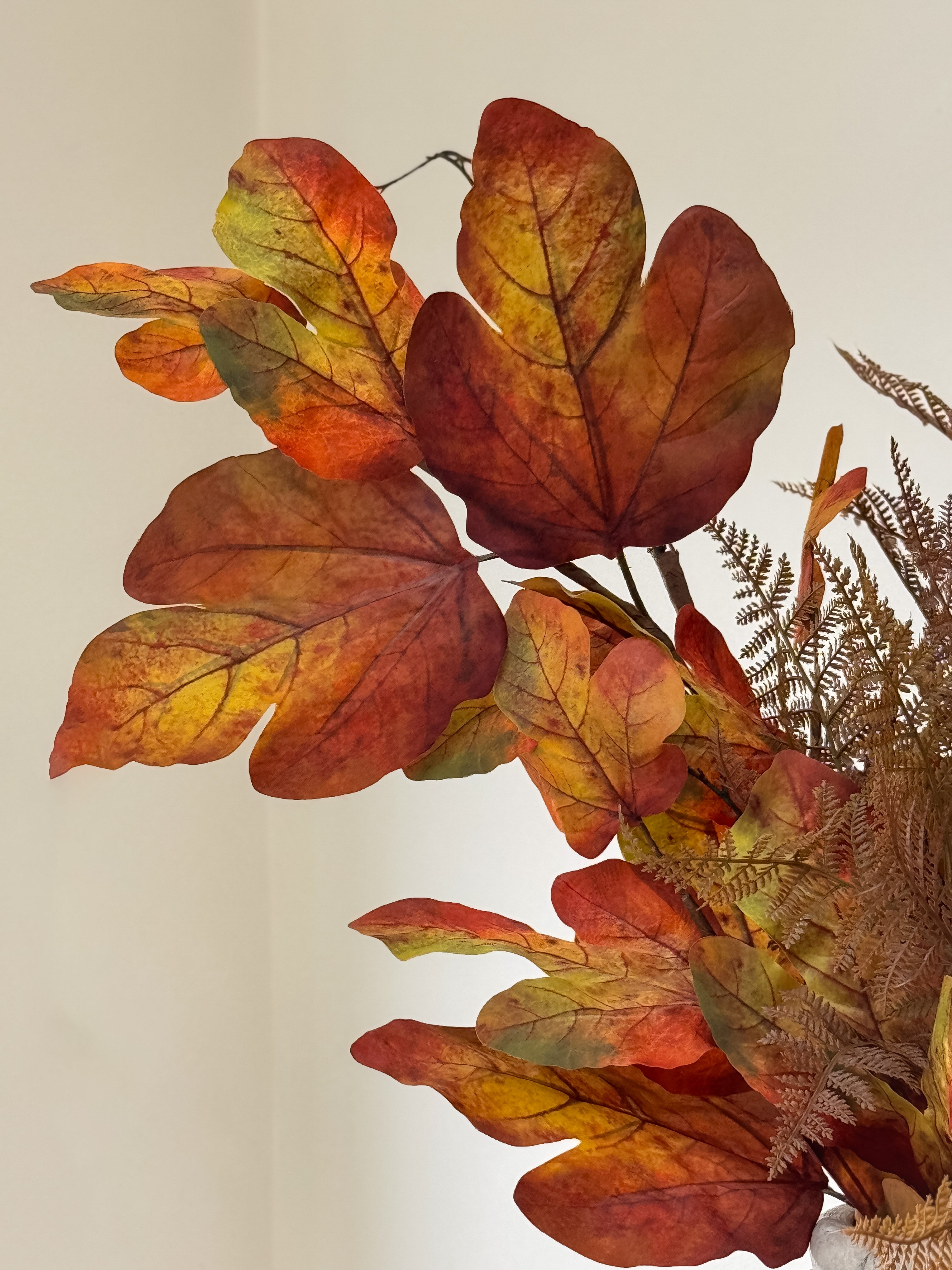 Artificial autumn leaf branch with red and orange leaves on a neutral background