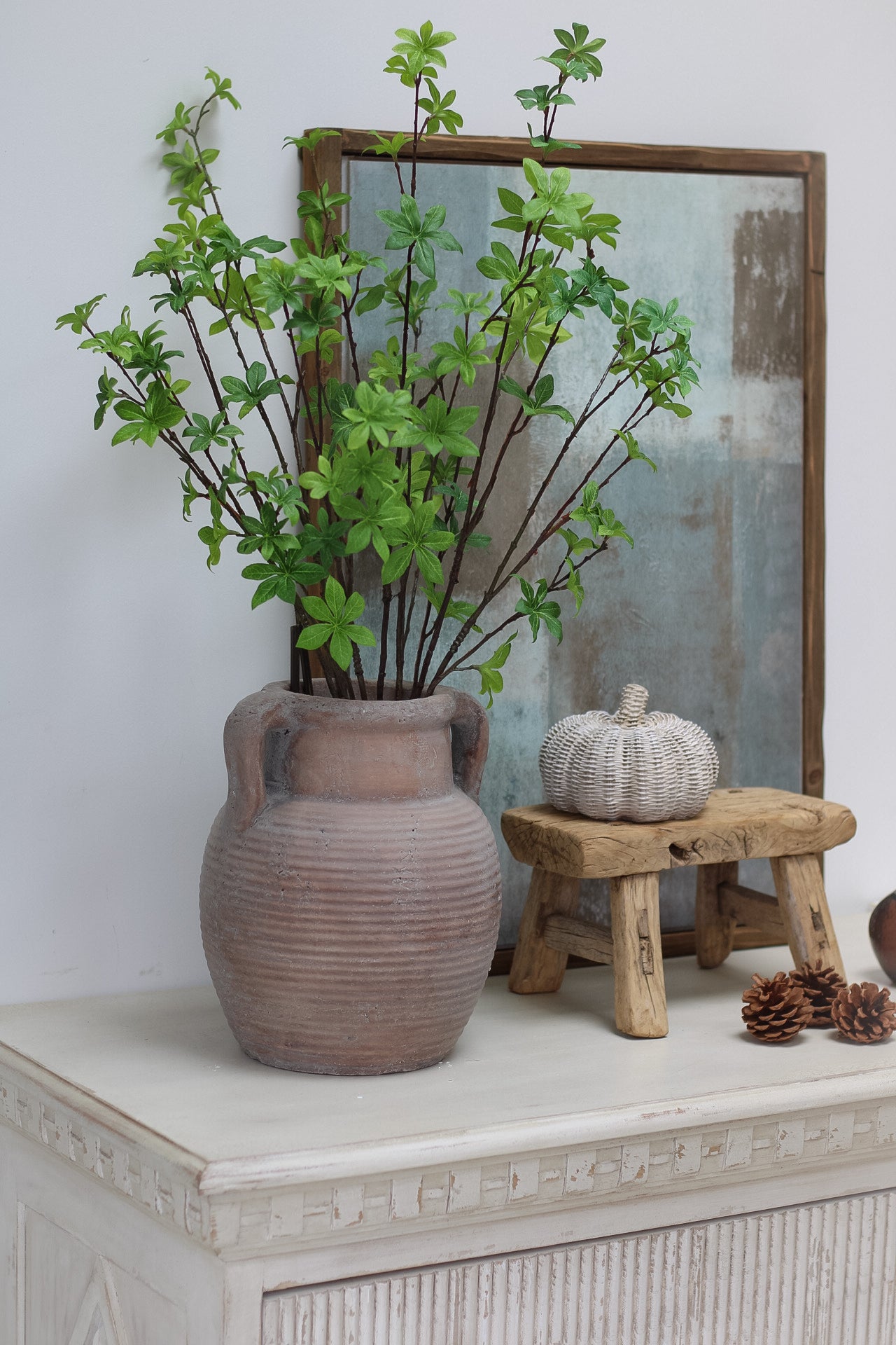 Decorative setting with a vase, Faux Green Enkianthus Spray and small pumpkin on a surface.