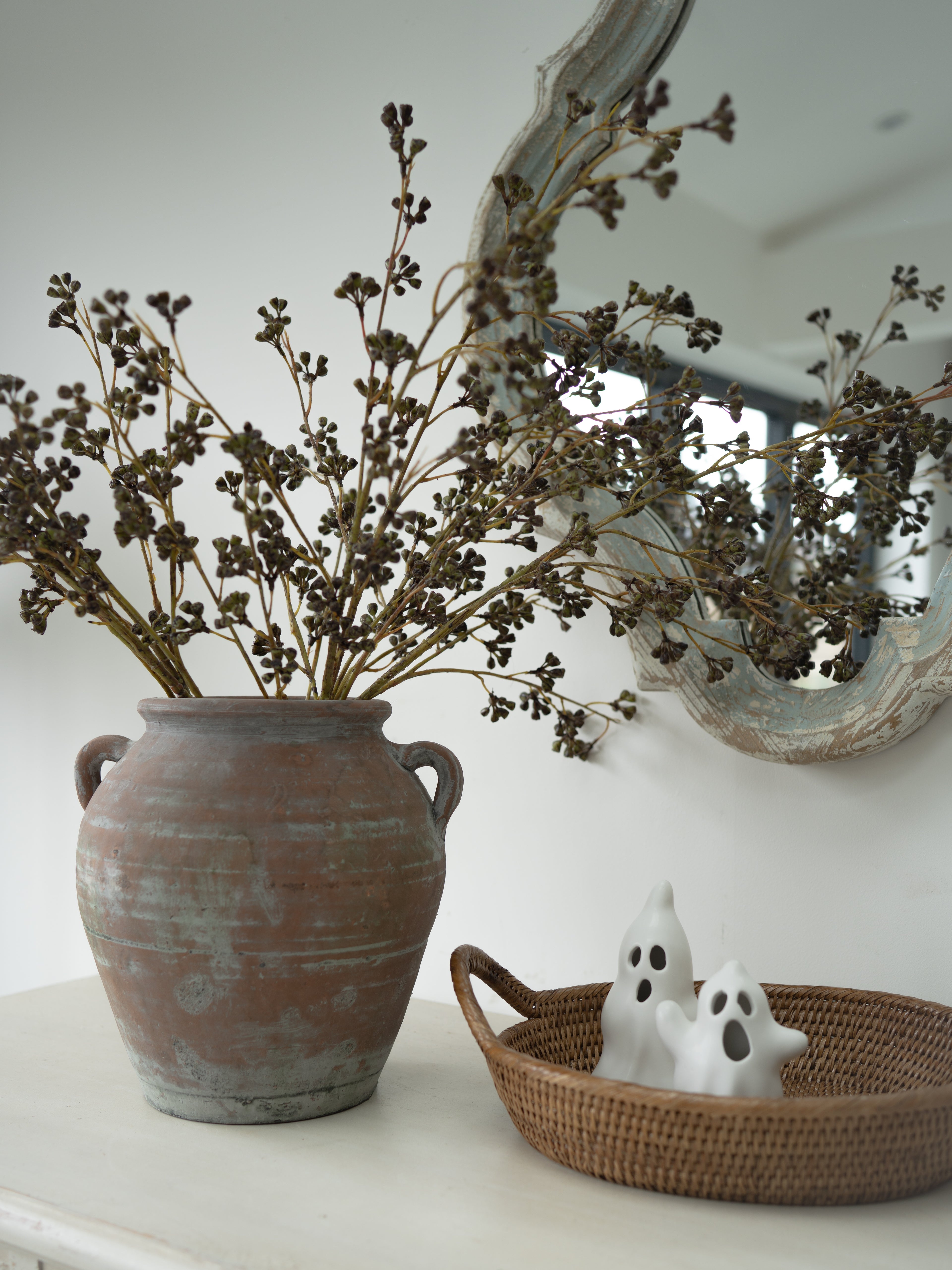 faux green huckleberry stems in vintage olive pot with oval rattan tray and white pair of ghost ornaments