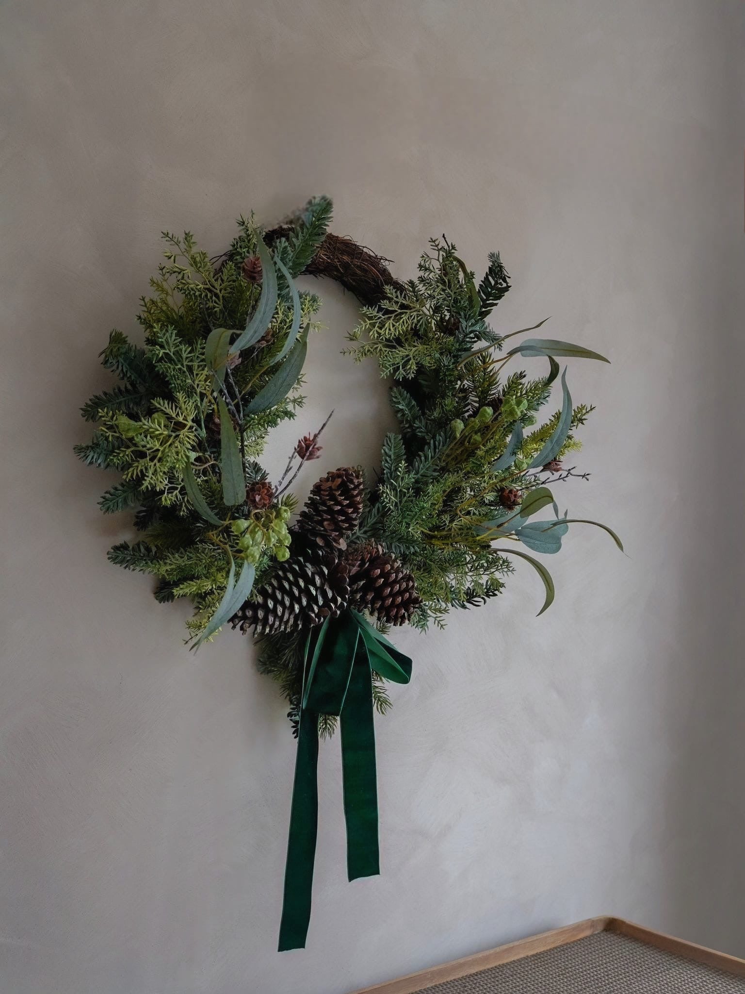 Christmas green faux foliage wreath with pinecones and a ribbon on a plain wall