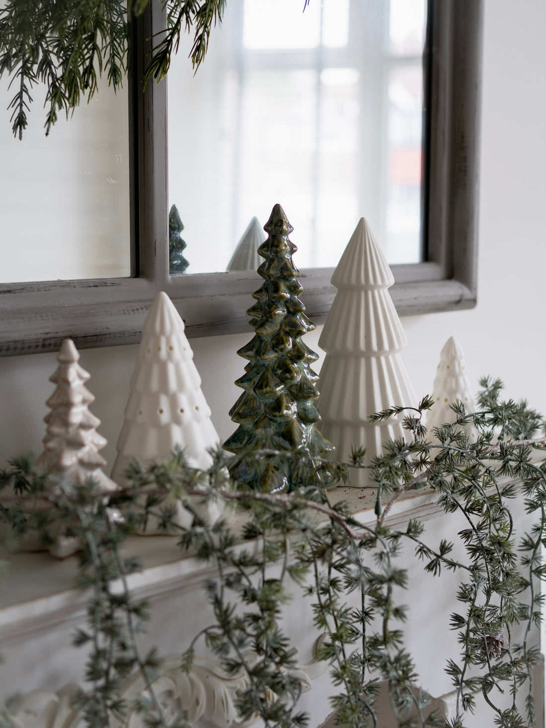 Decorative ceramic Christmas trees on a mantelpiece with a mirror in the background.