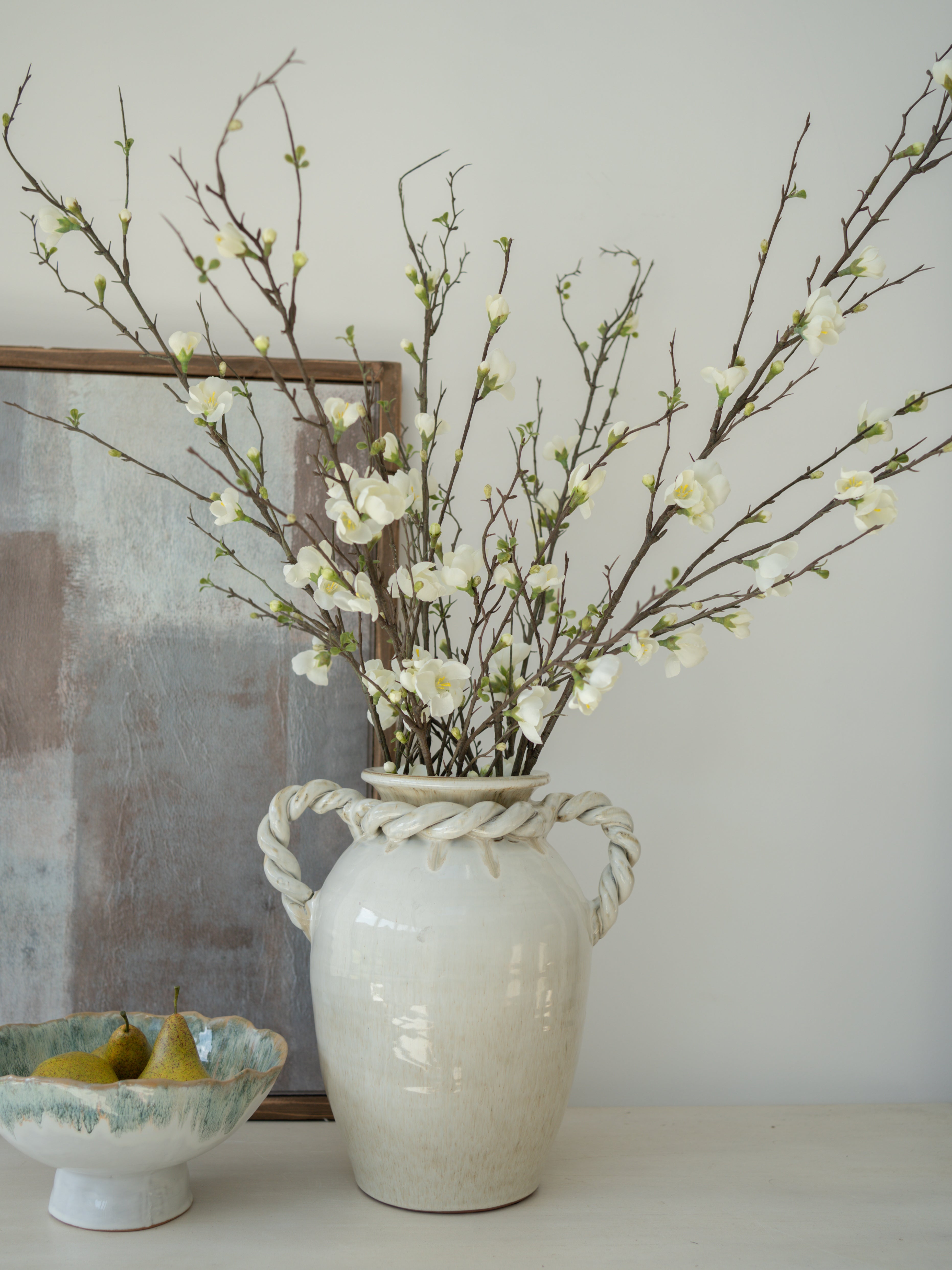 White vase with branches and blossom flowers on a neutral background
