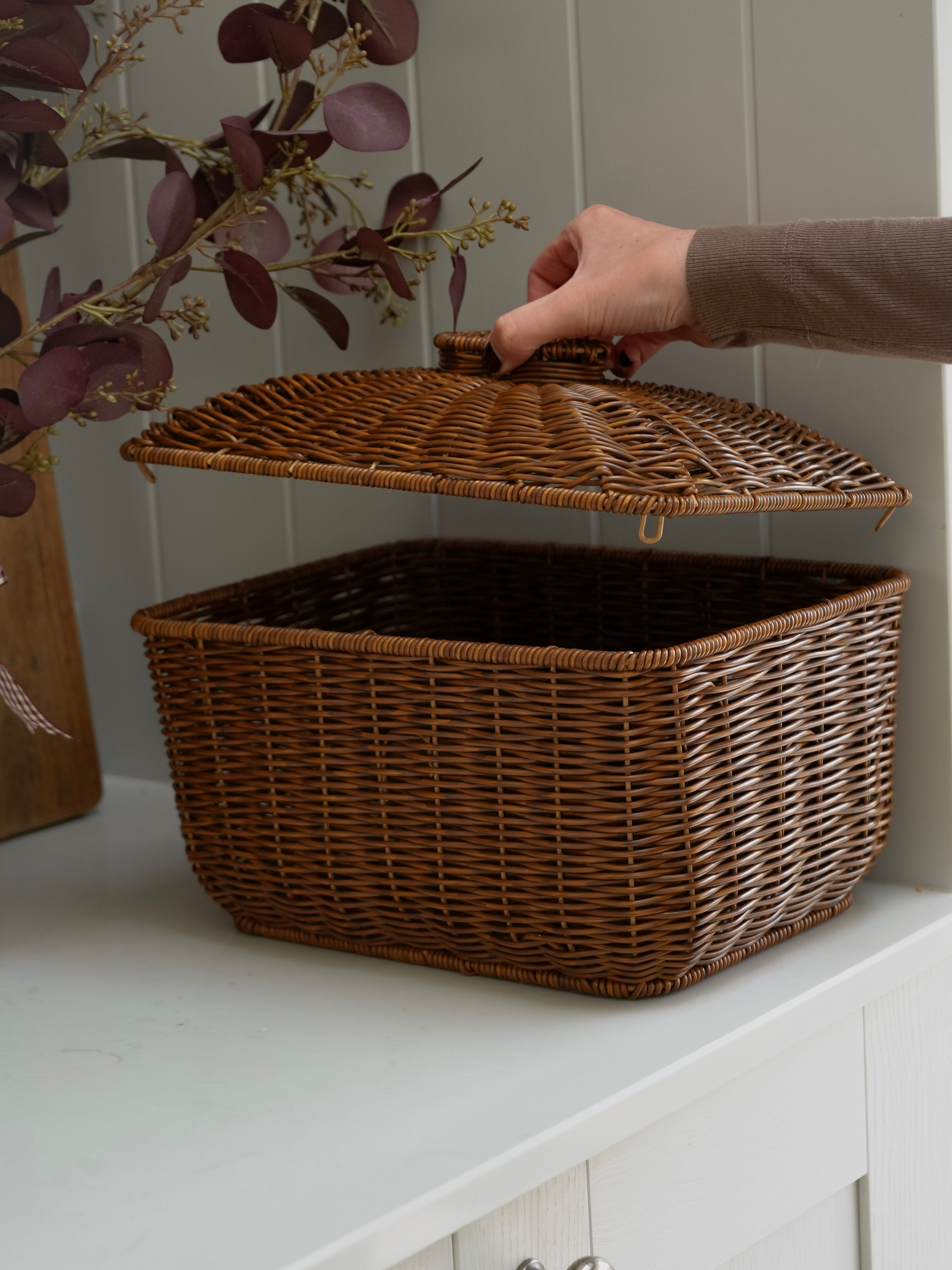 Wicker storage basket with a lid on a white surface, held by a hand.