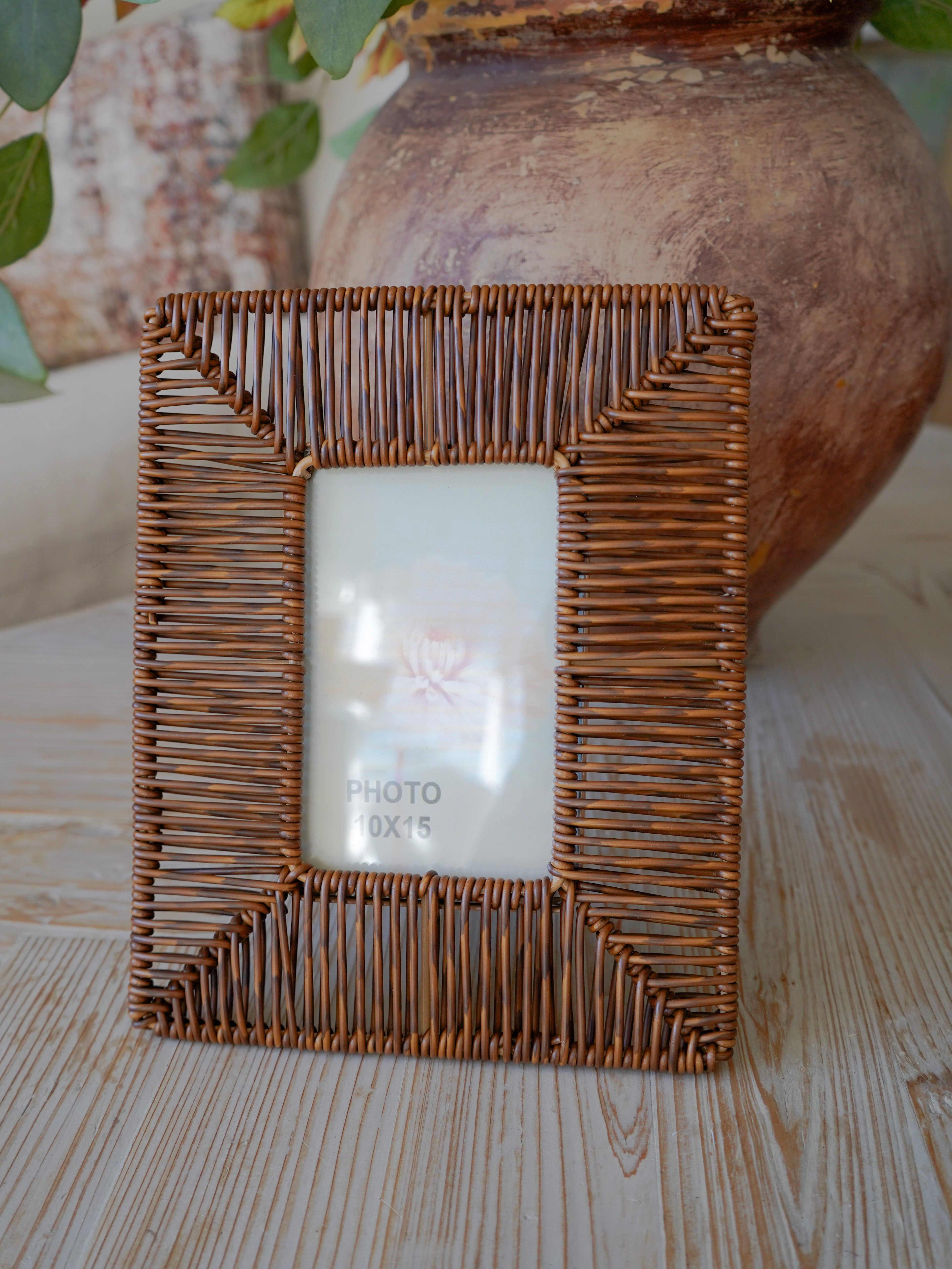 Wicker picture frame on a wooden surface with a blurred vase in the background