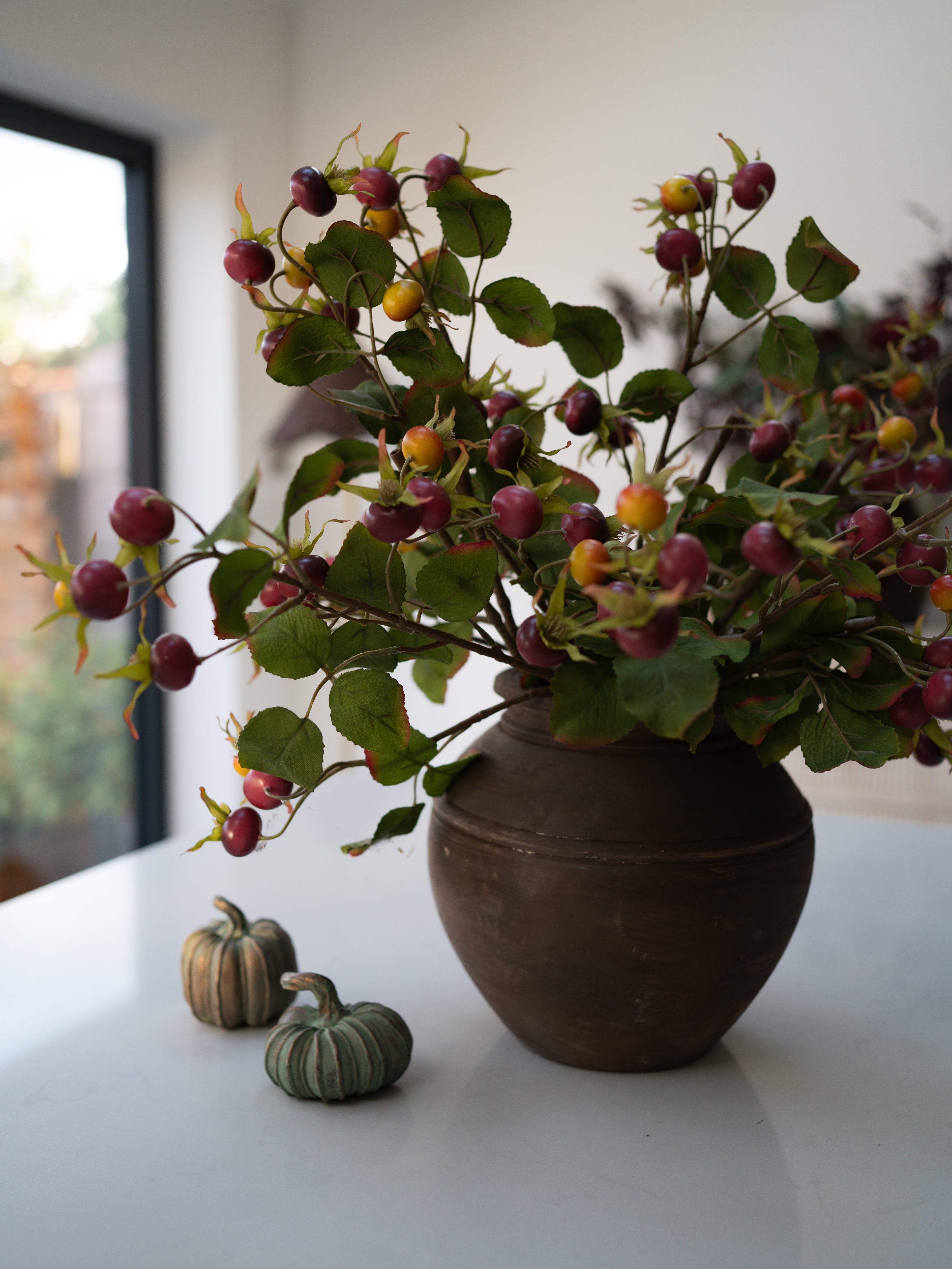 Faux Rosehip Branch in brown rustic vase with decorative verdigris pumpkins