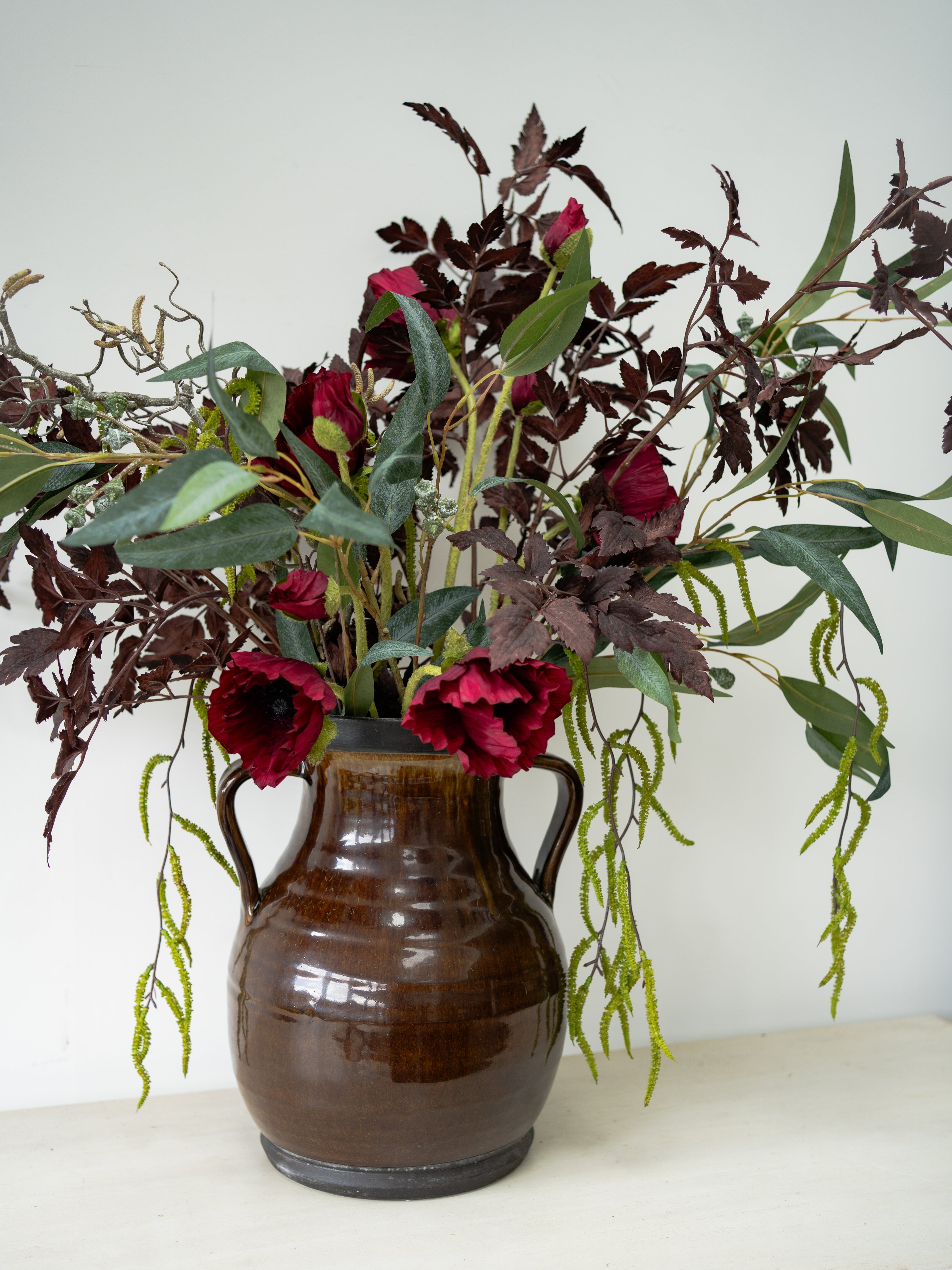 Brown ceramic vase with whimsical red flowers and green leaves on a white surface