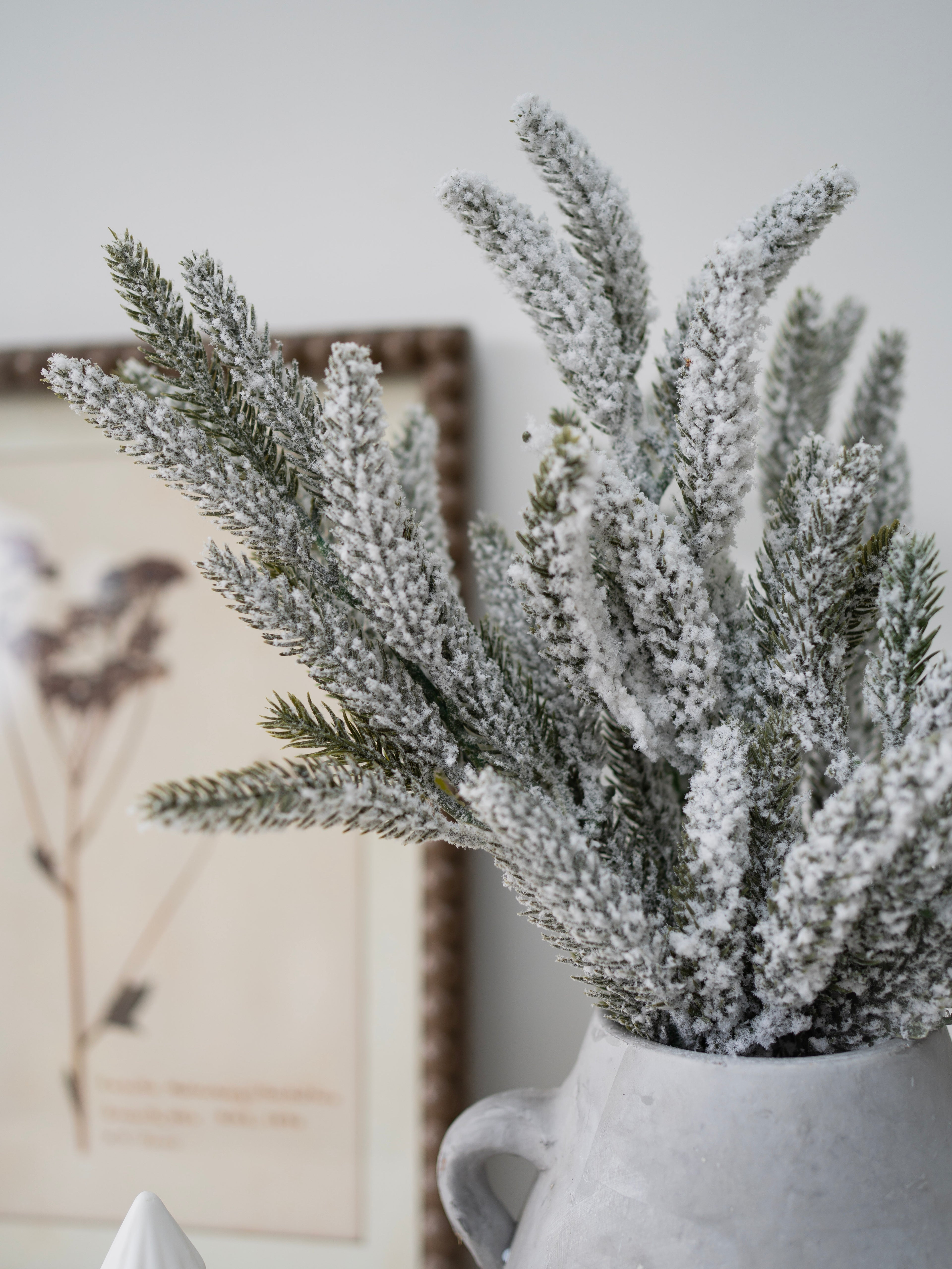 Frosted artificial plants in a white vase against a neutral background