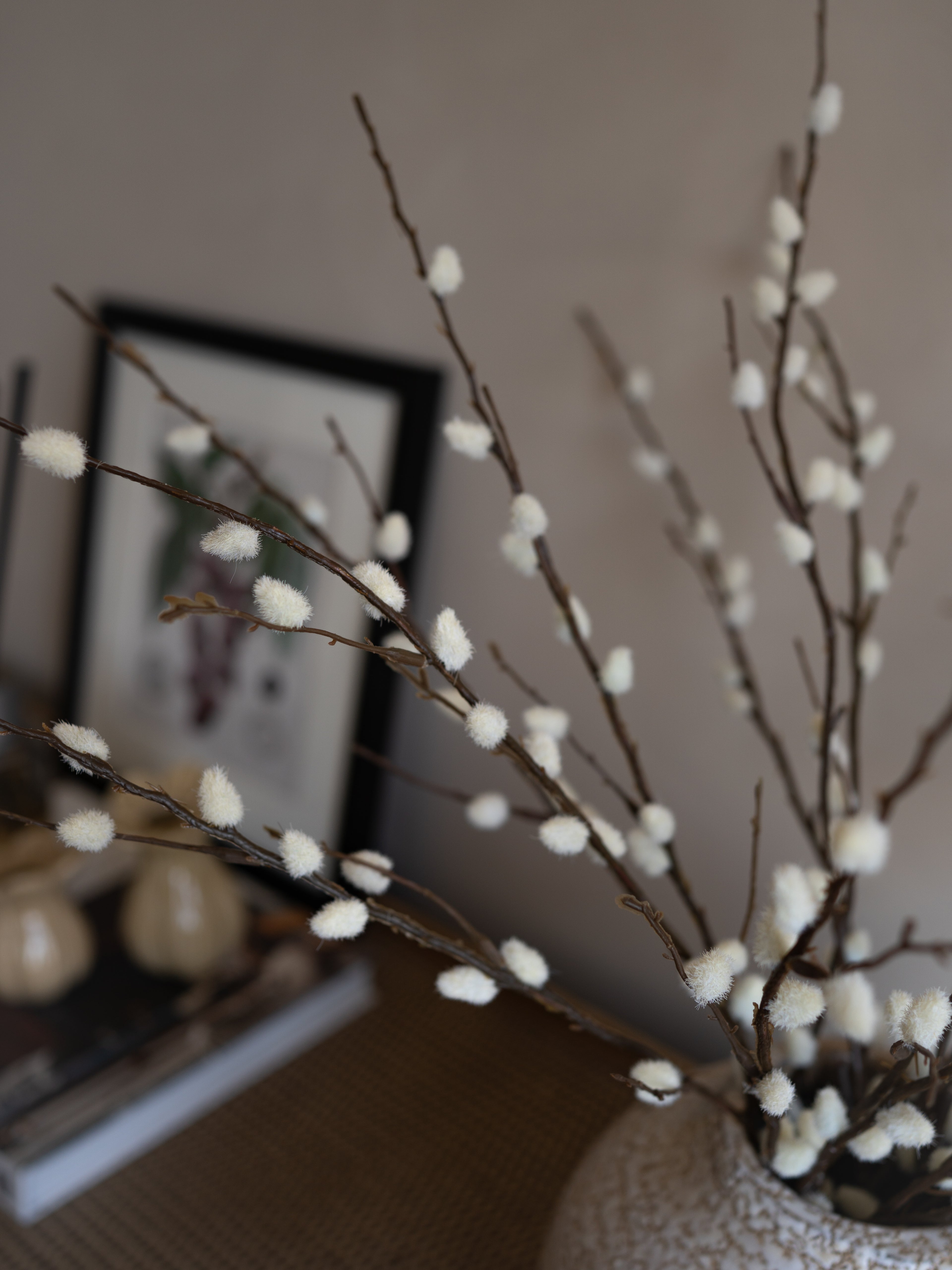 Decorative willow branches with white buds in a vase against a neutral background