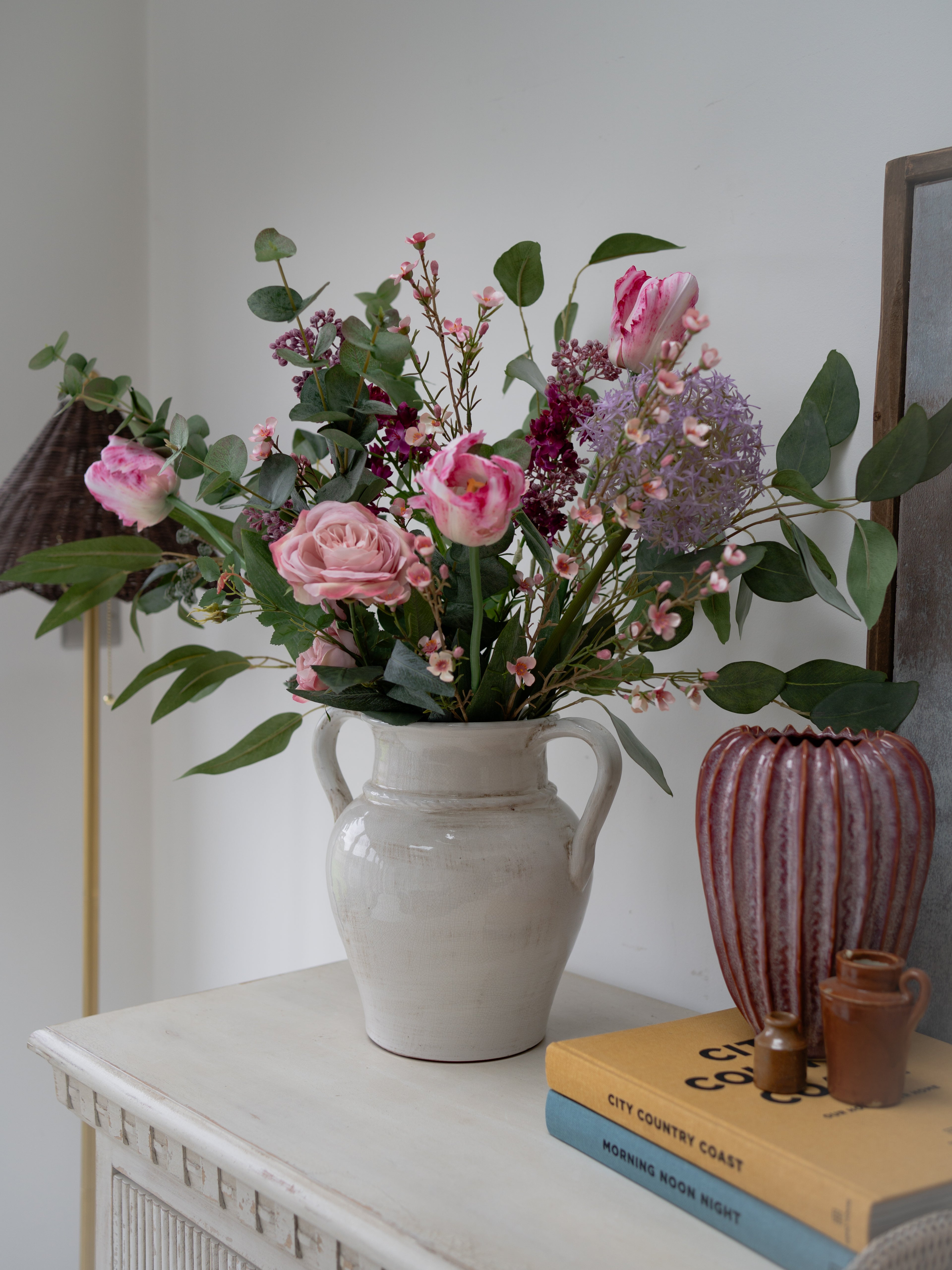 Floral arrangement in a white vase on a surface with books and another vase.