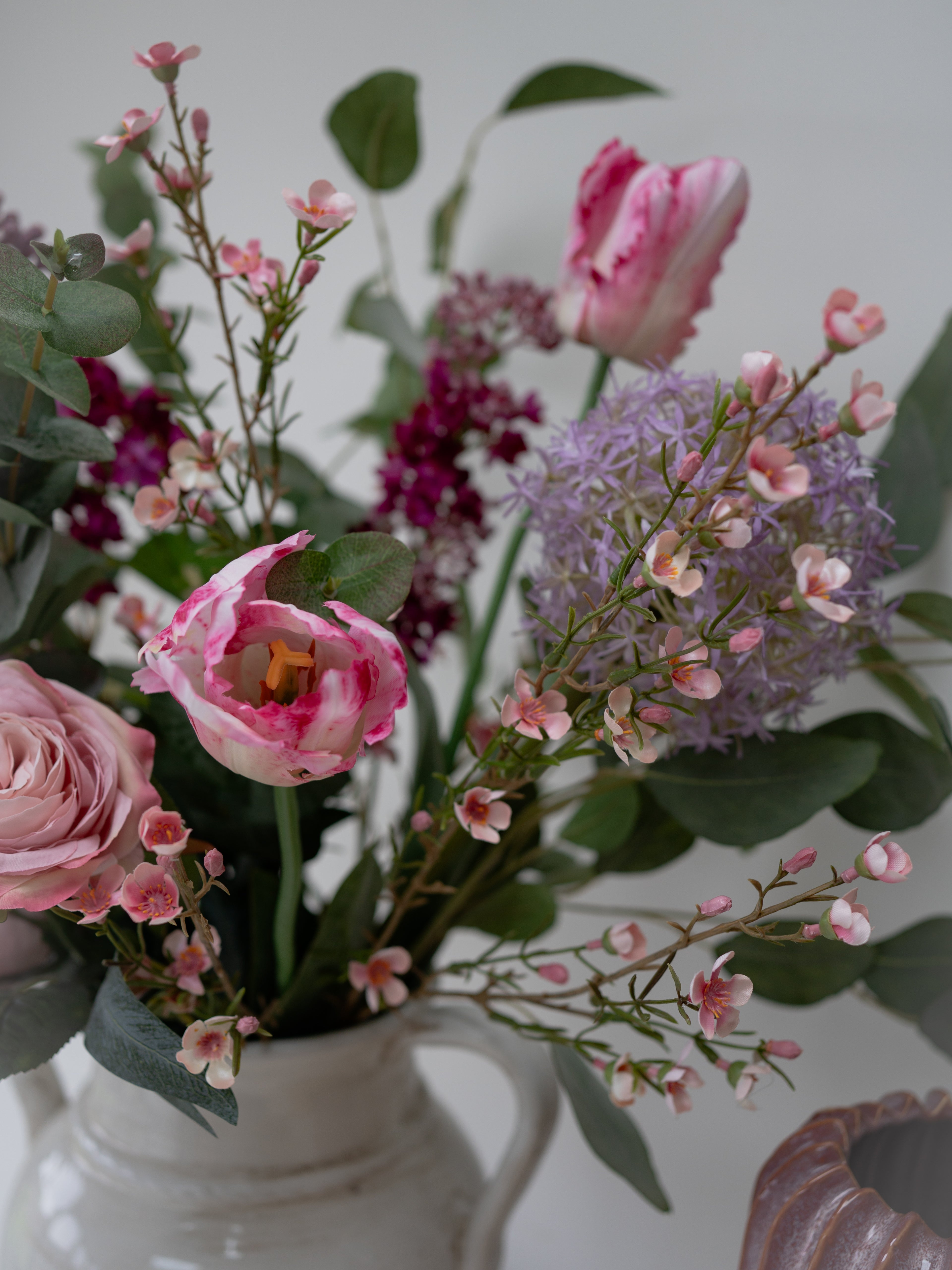 Bouquet of pink and purple flowers in a white vase against a neutral background
