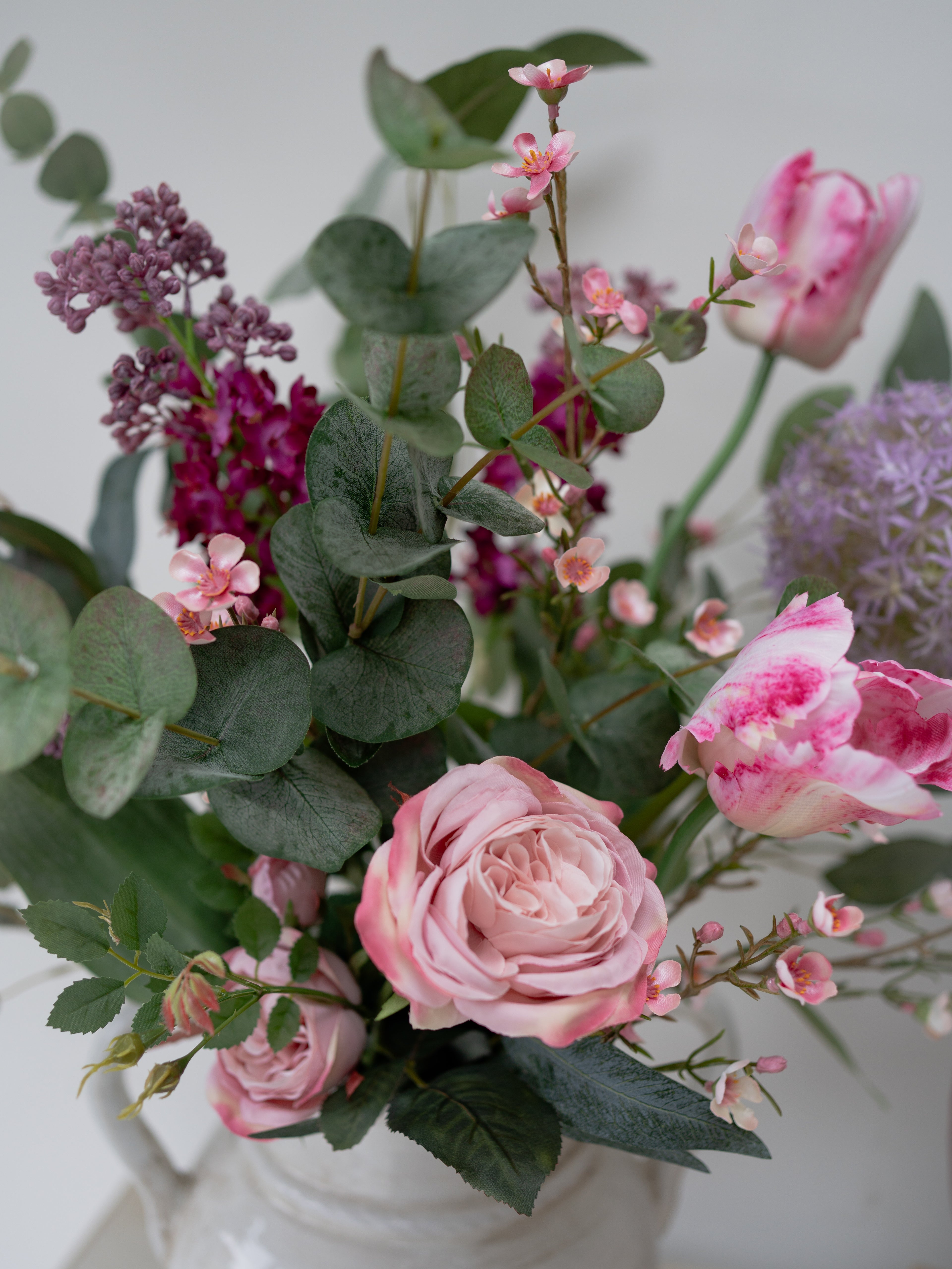 Bouquet of pink roses and other flowers in a white vase against a light background