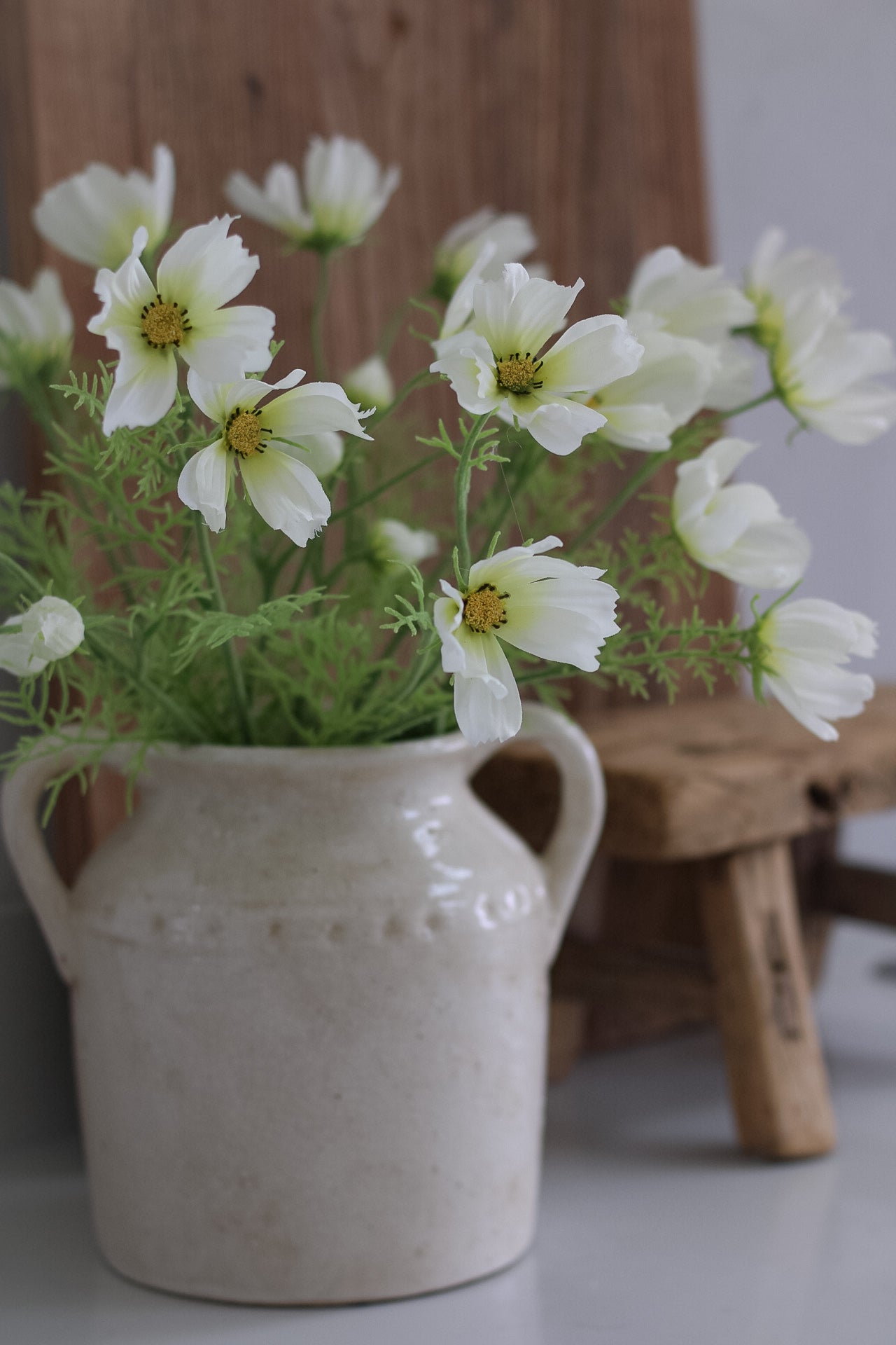 faux White cosmos flowers in a ceramic vase on a wooden surface