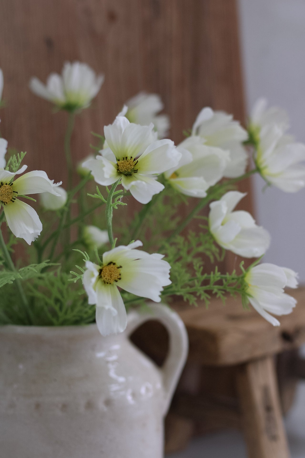 faux White cosmos flowers in a white vase on a wooden surface