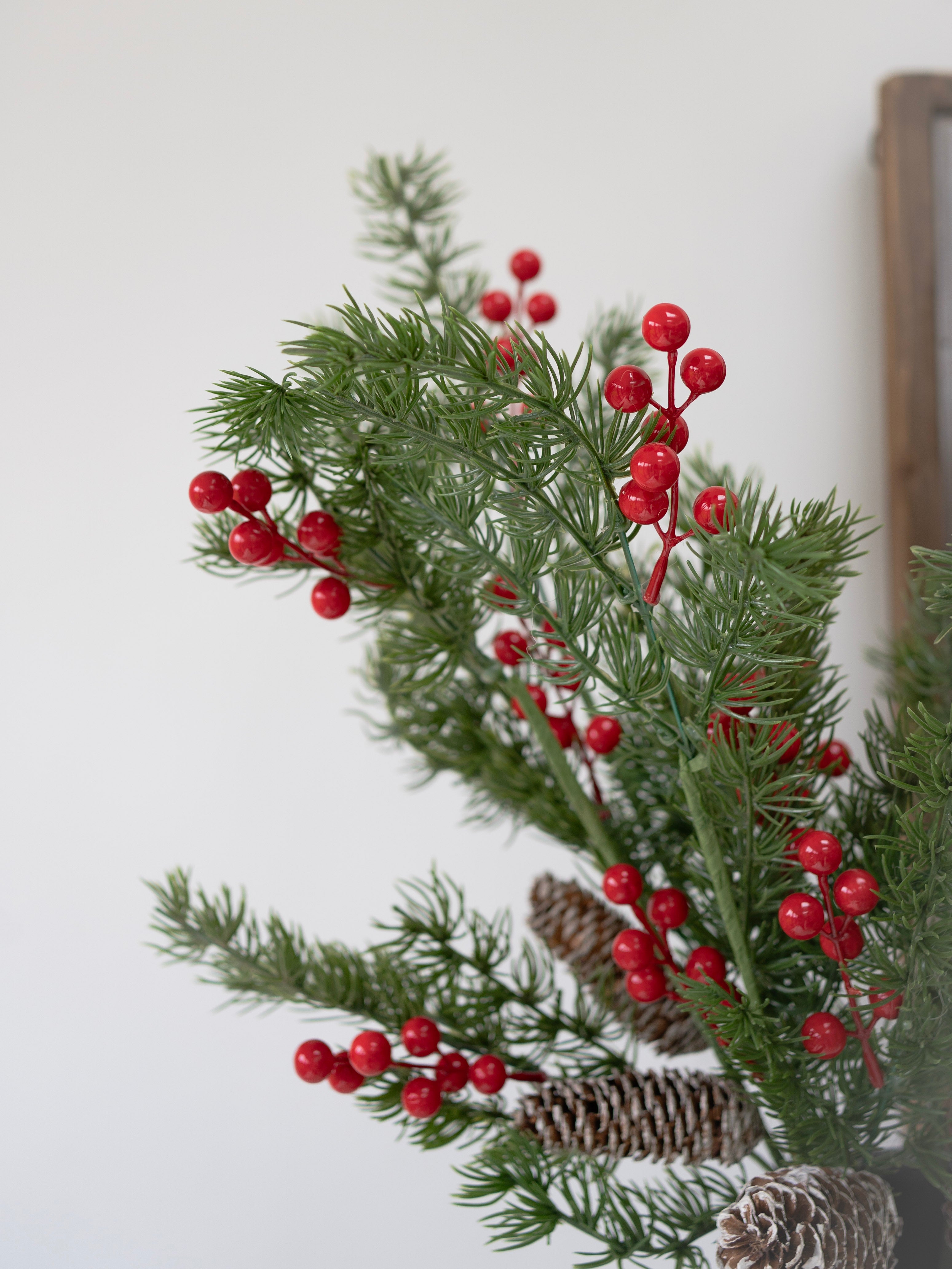 Decorative faux christmas foliage arrangement with red berries and pine cones on a white background