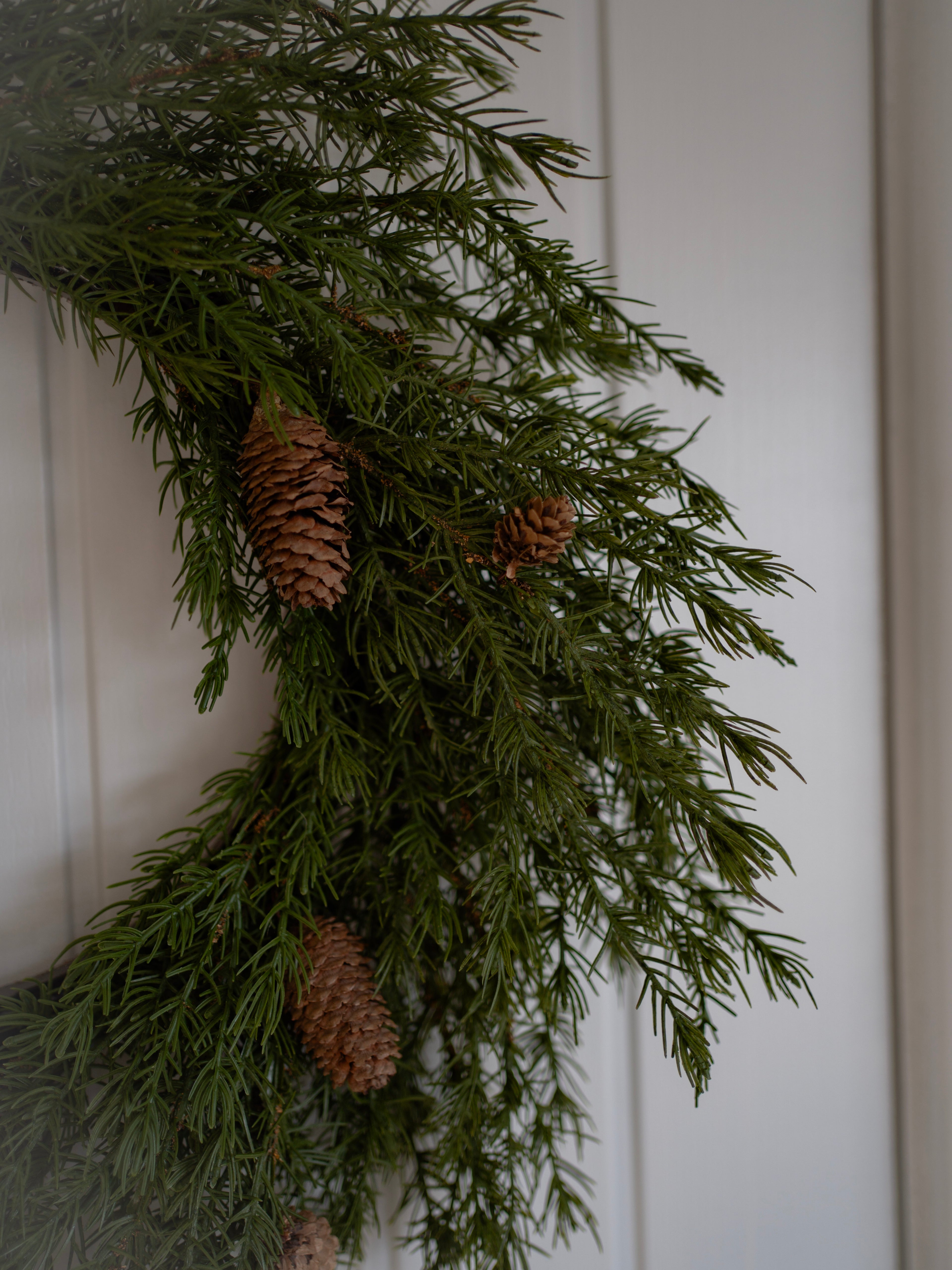 faux woodland wreath with pine cones on a white paneled wall