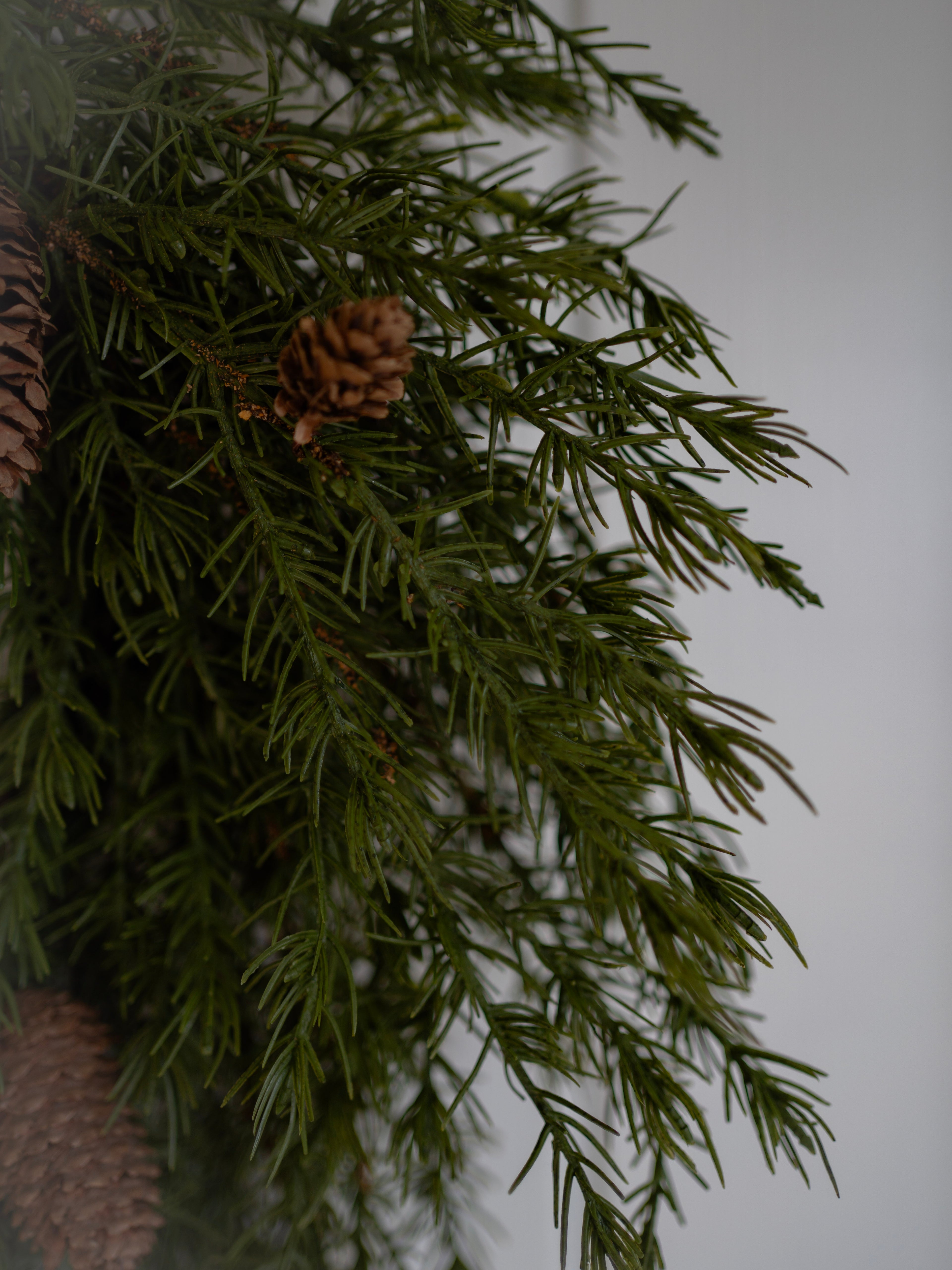 Close-up of faux green pine wreath with pinecones on a white background