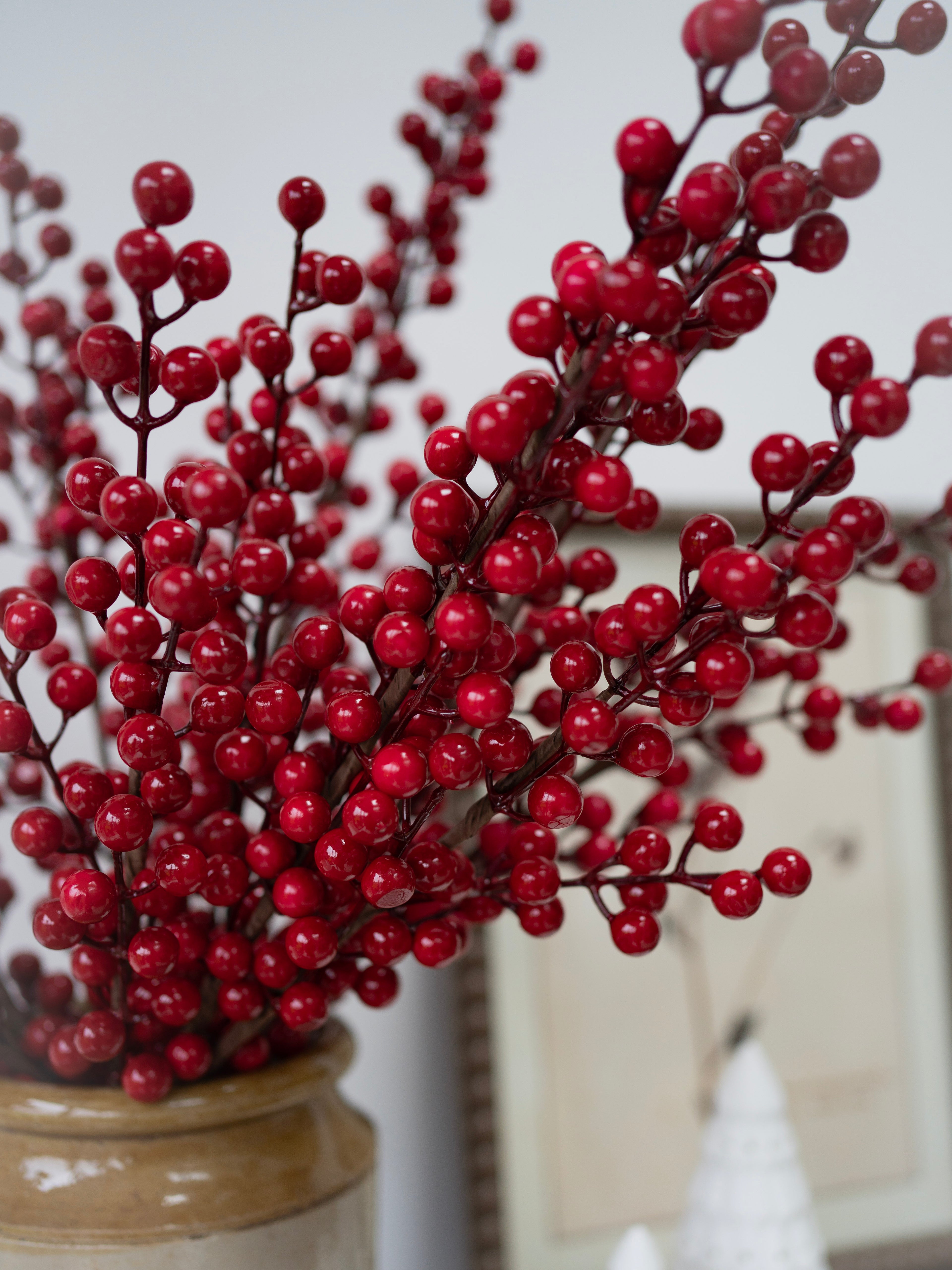Faux red berry branches in a vase against a neutral background