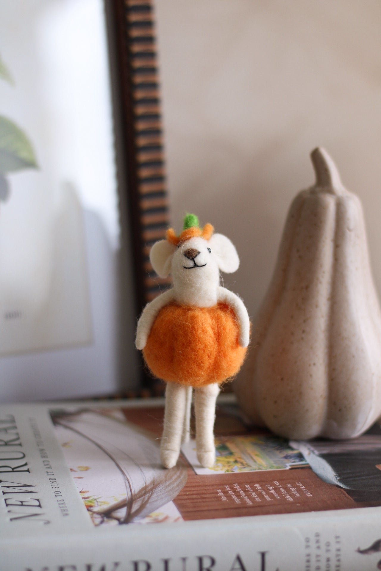 Small plush toy dressed in a pumpkin costume on a surface with a newspaper and gourd in the background.