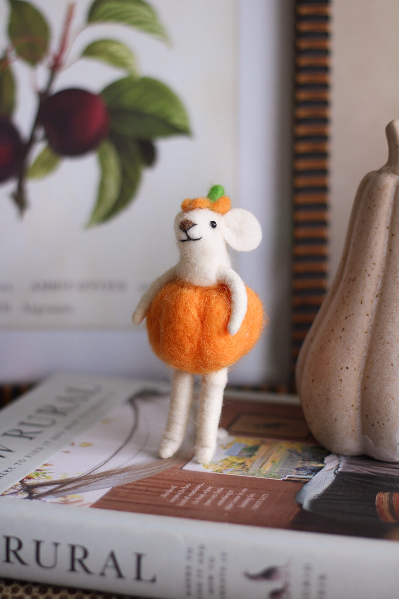 Small felt mouse figurine with an orange pumpkin dress on a surface with a book and decorative items in the background.