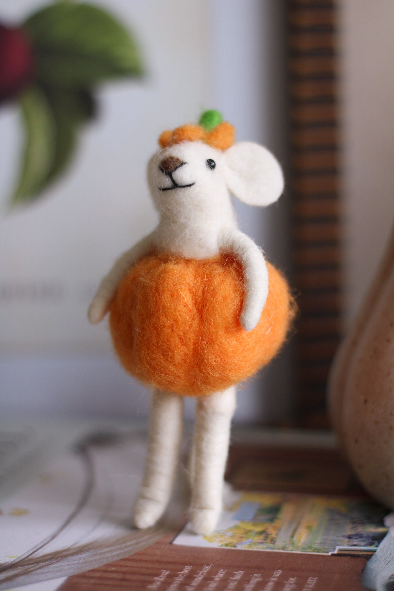 Small plush toy mouse in an orange dress with a green leaf on a surface.