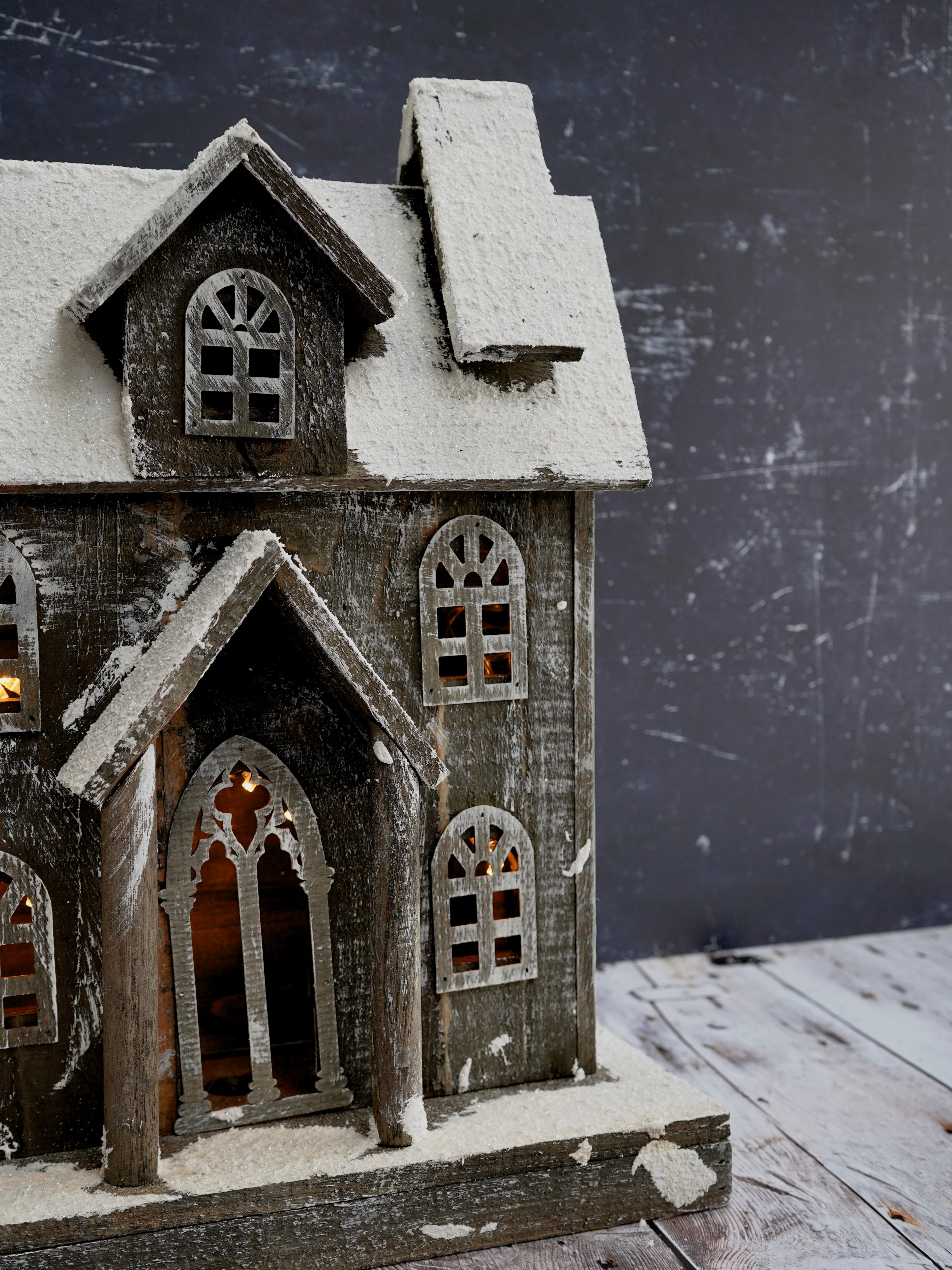 Decorative model of a gothic-style house with snow on the roof against a dark background.