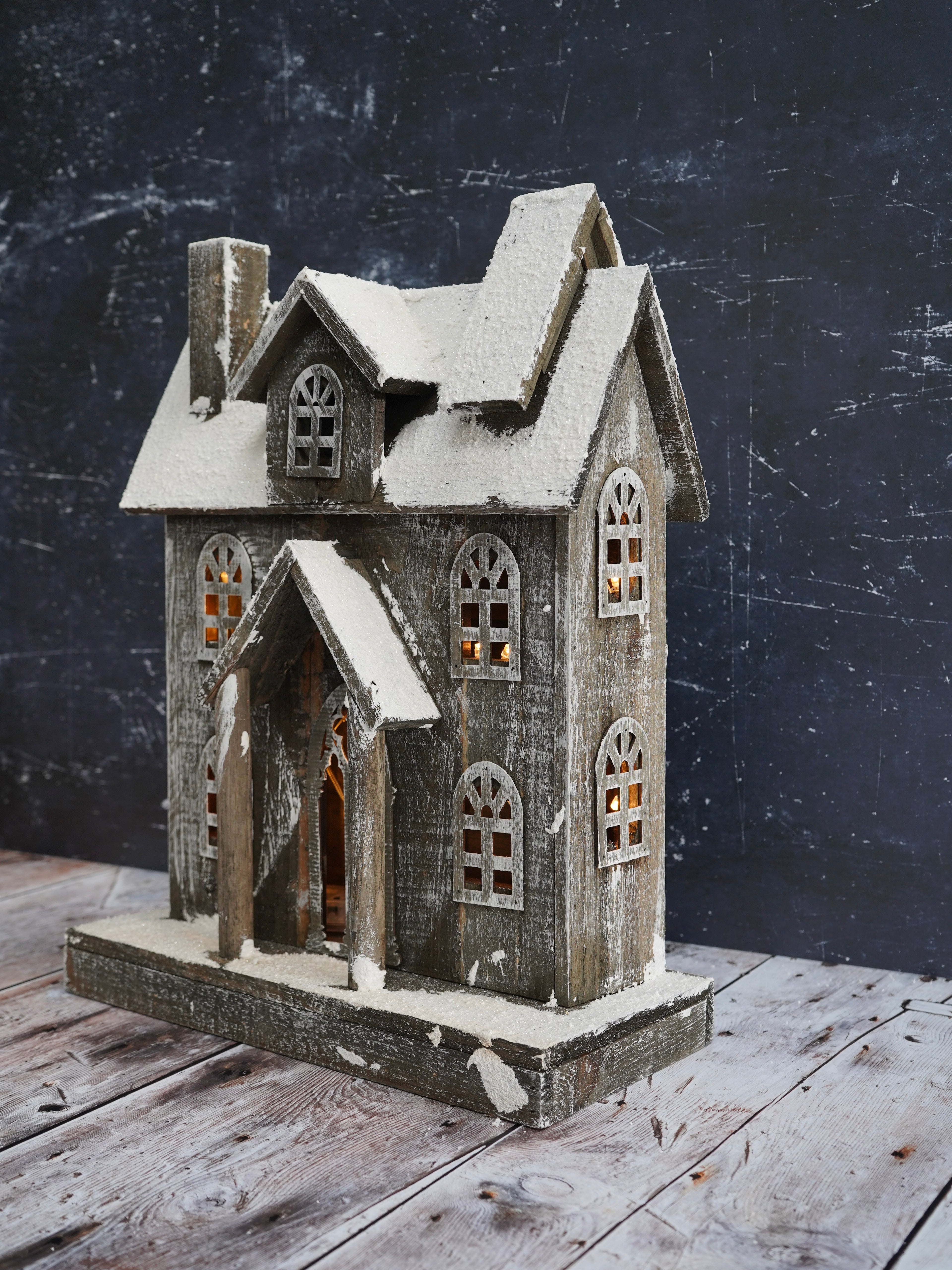Decorative model of a house with snow on a wooden surface and dark background