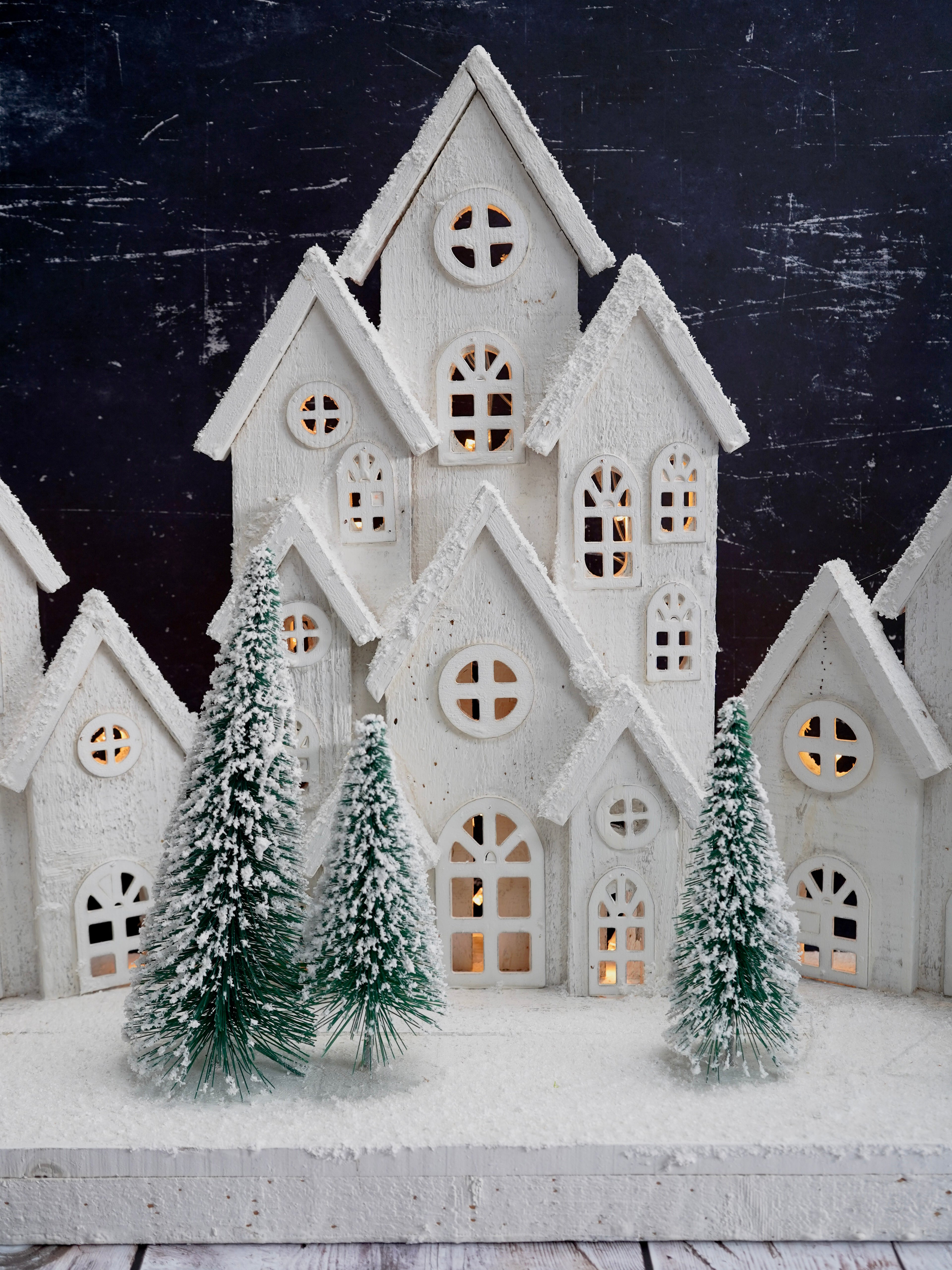 Decorative white house with lit windows and snow-covered trees against a dark background