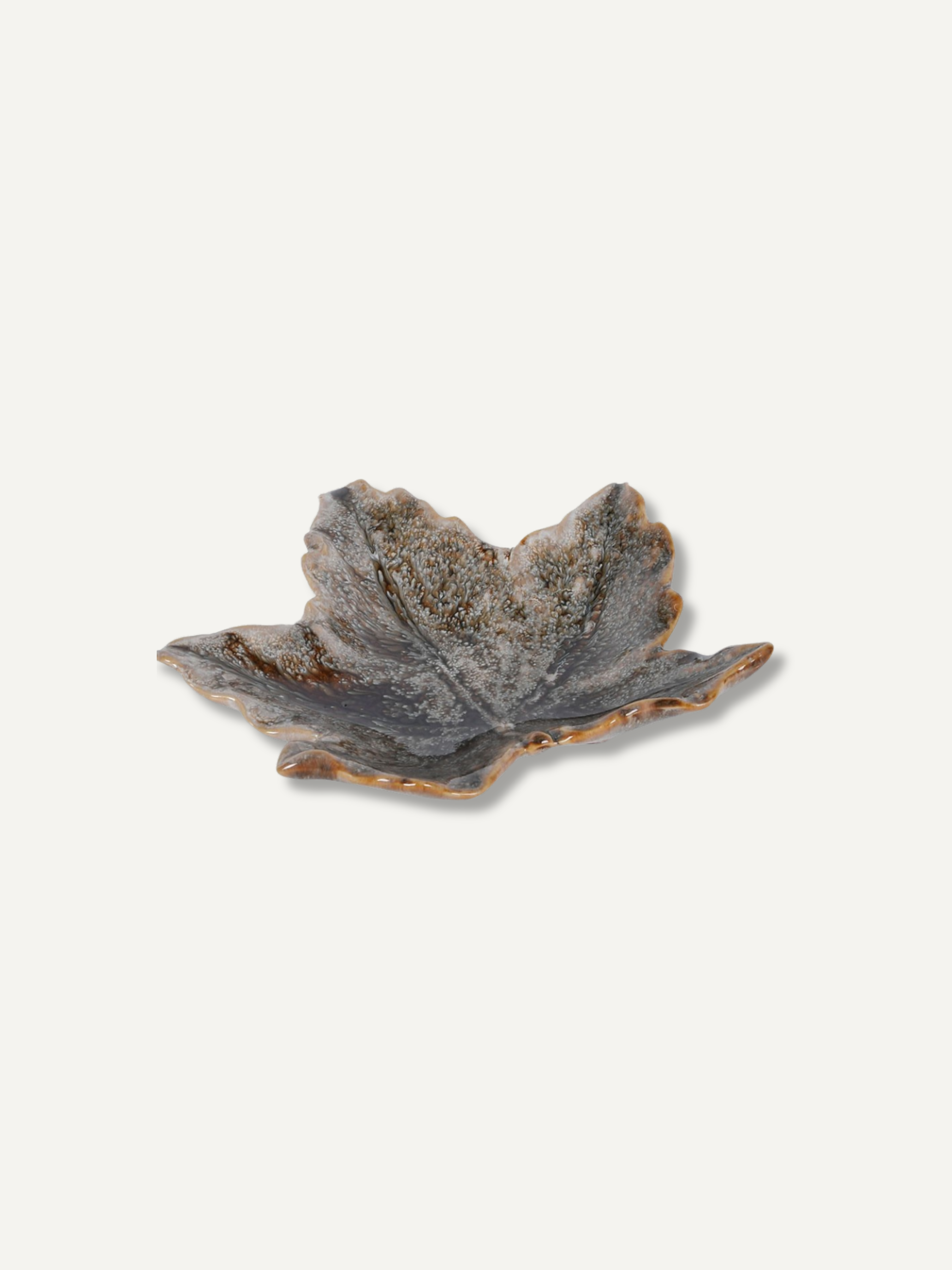A small leaf-shaped ceramic dish with a textured, speckled glaze in earthy gray, brown, and beige tones, set against a solid off-white background.