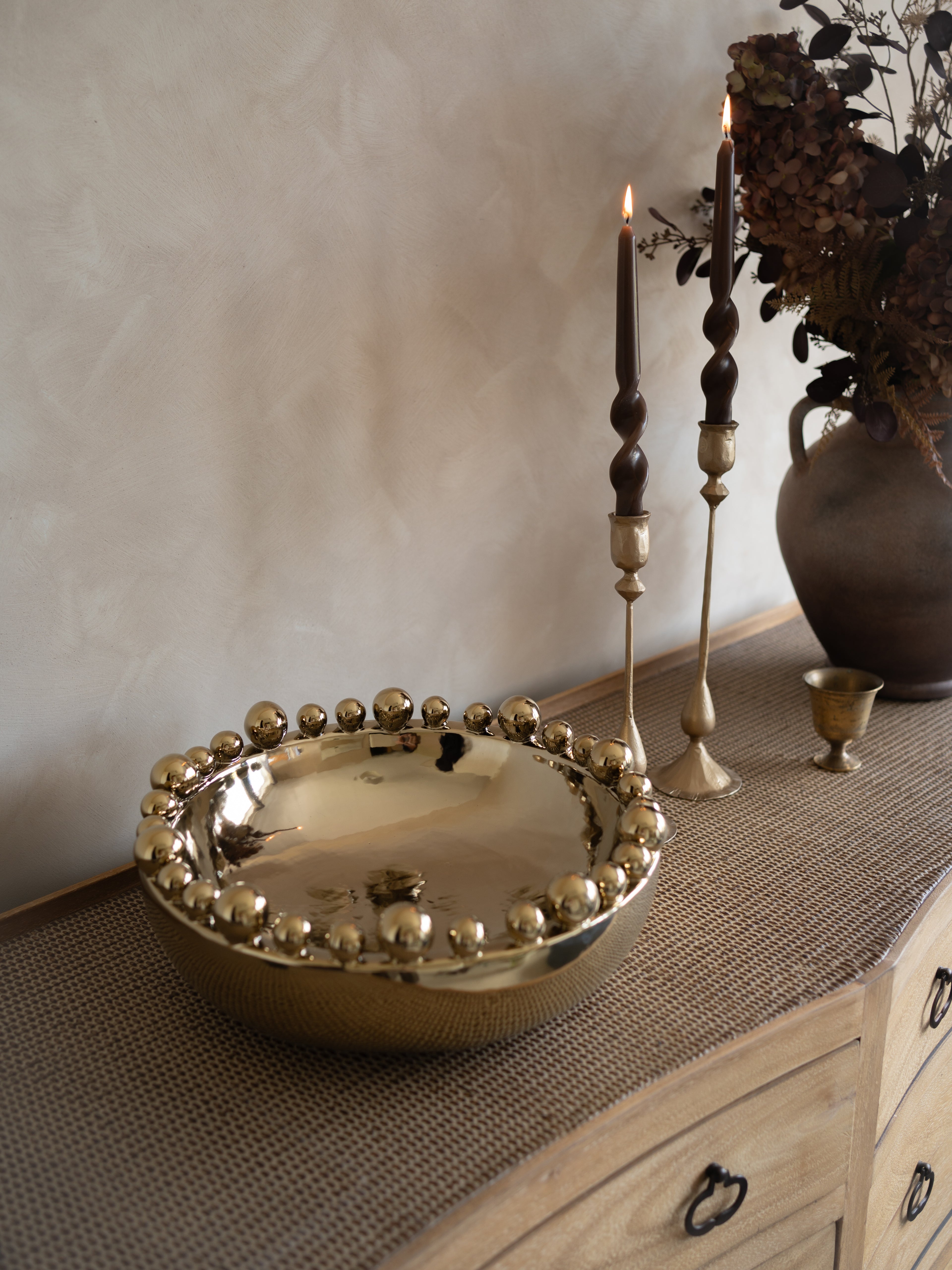 Decorative bowl with spherical design on a textured surface with candles and a vase.