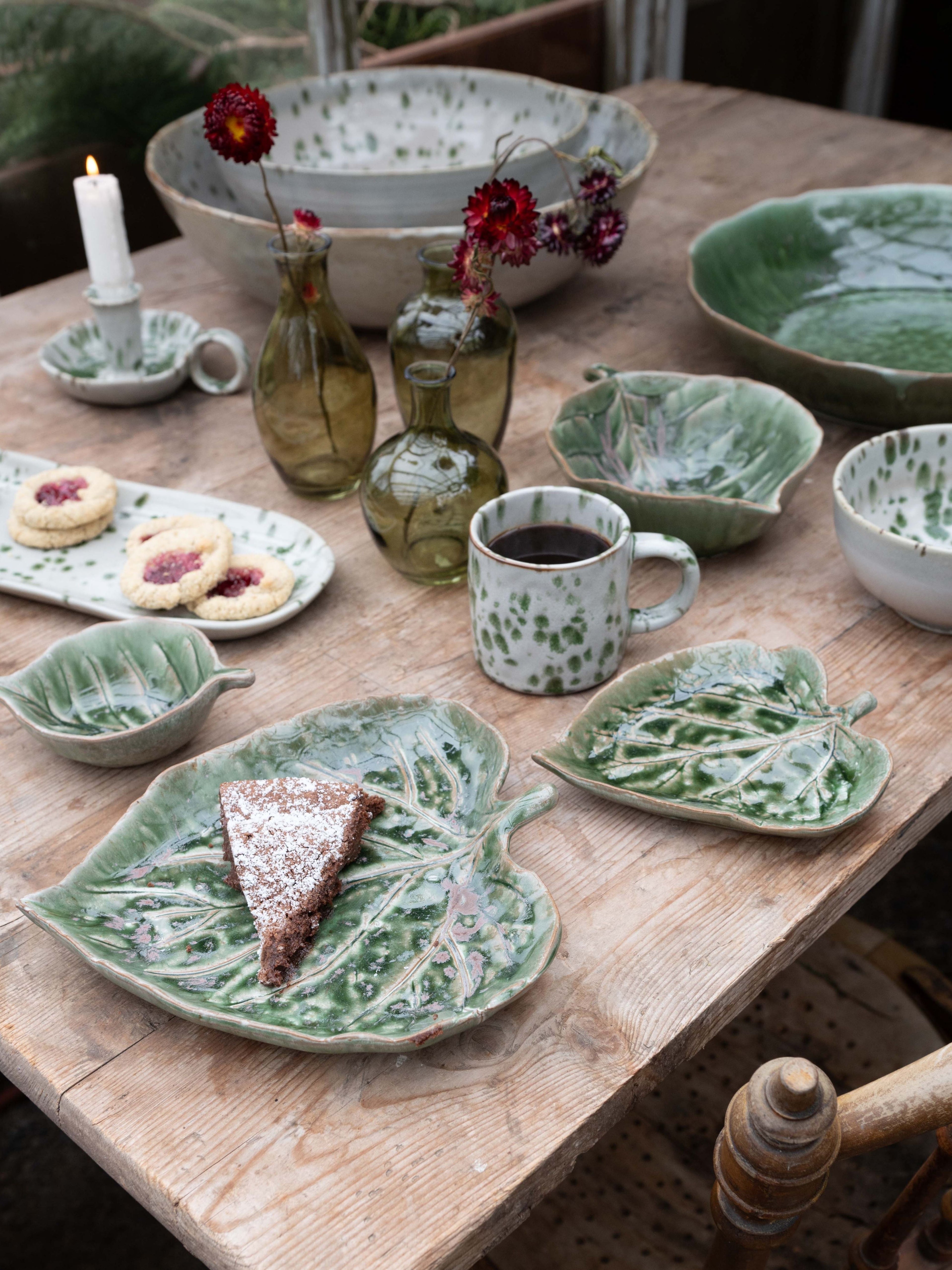 Ceramic tableware including bowls, plates, and mugs on a wooden table with a rustic setting.