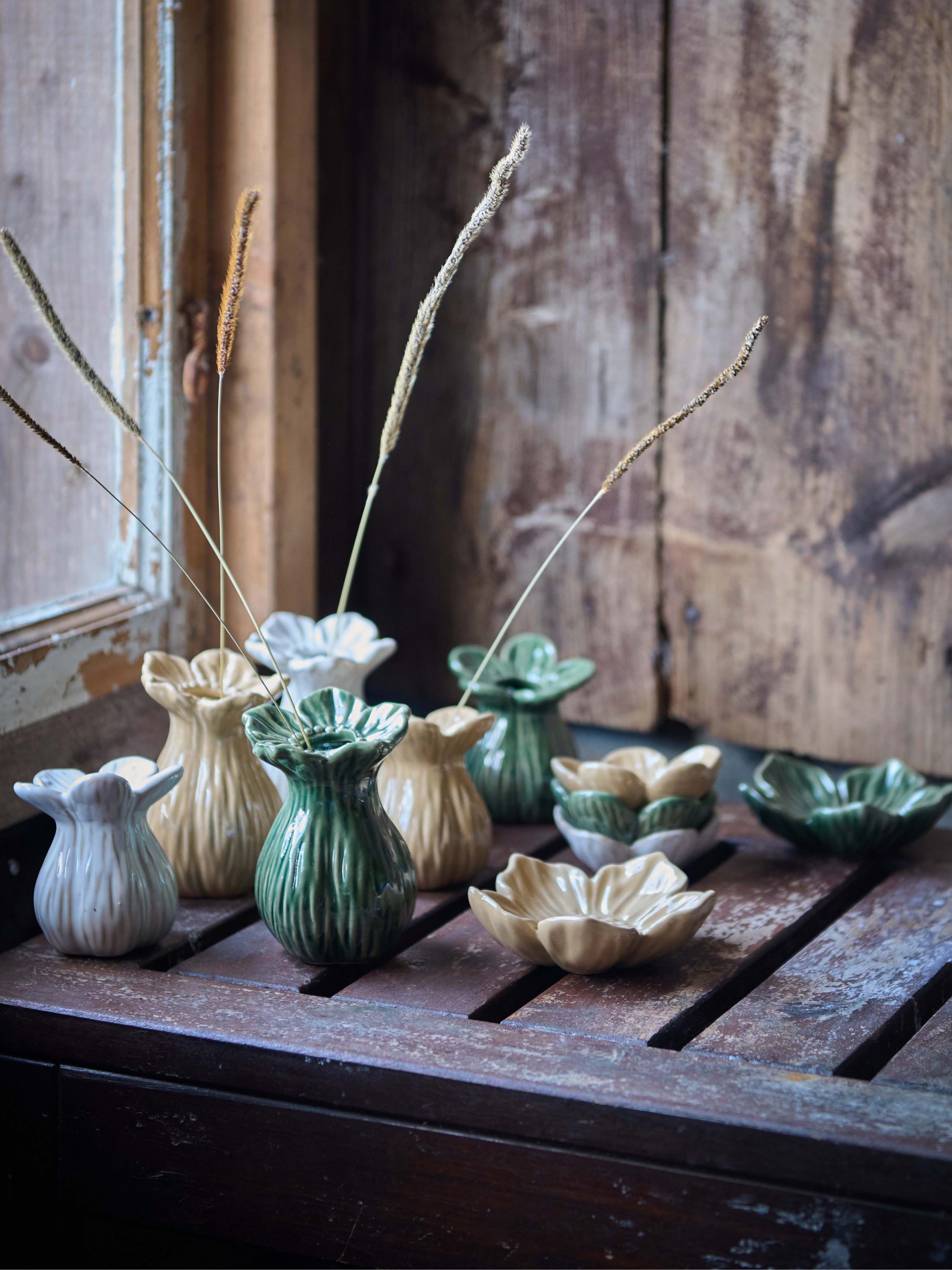 Collection of small ceramic bud vases and bowls on a wooden surface with a rustic background.