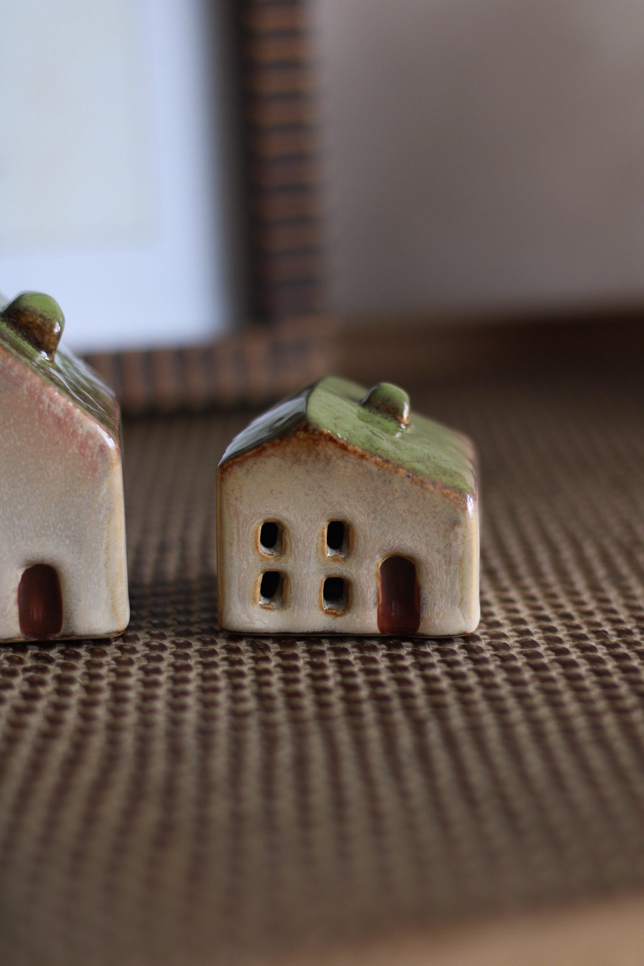 Two small ceramic houses with green roofs on a textured surface.