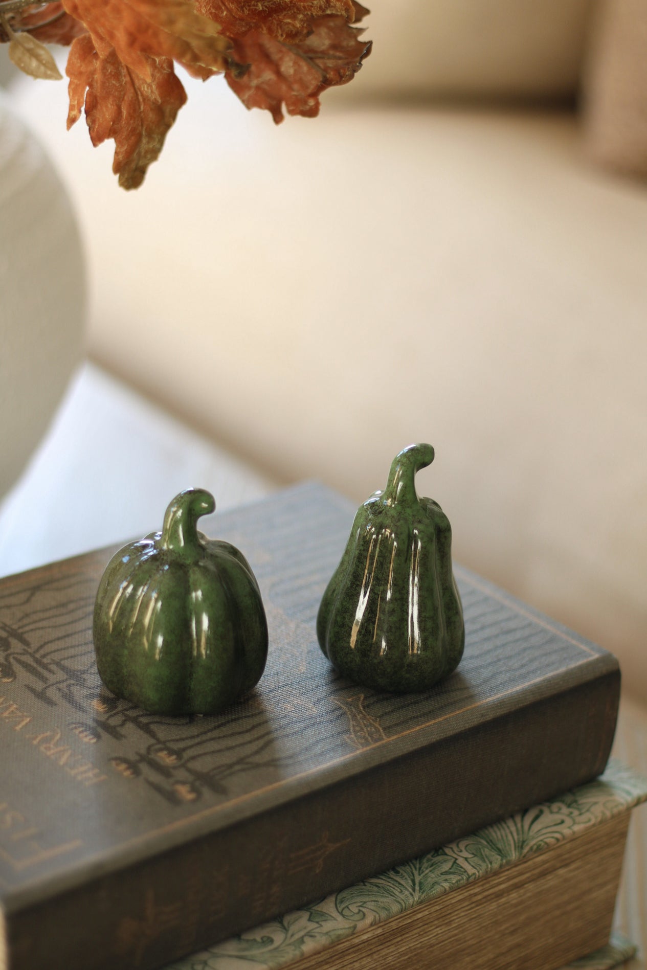 Two green ceramic pumpkins on a book with a blurred background