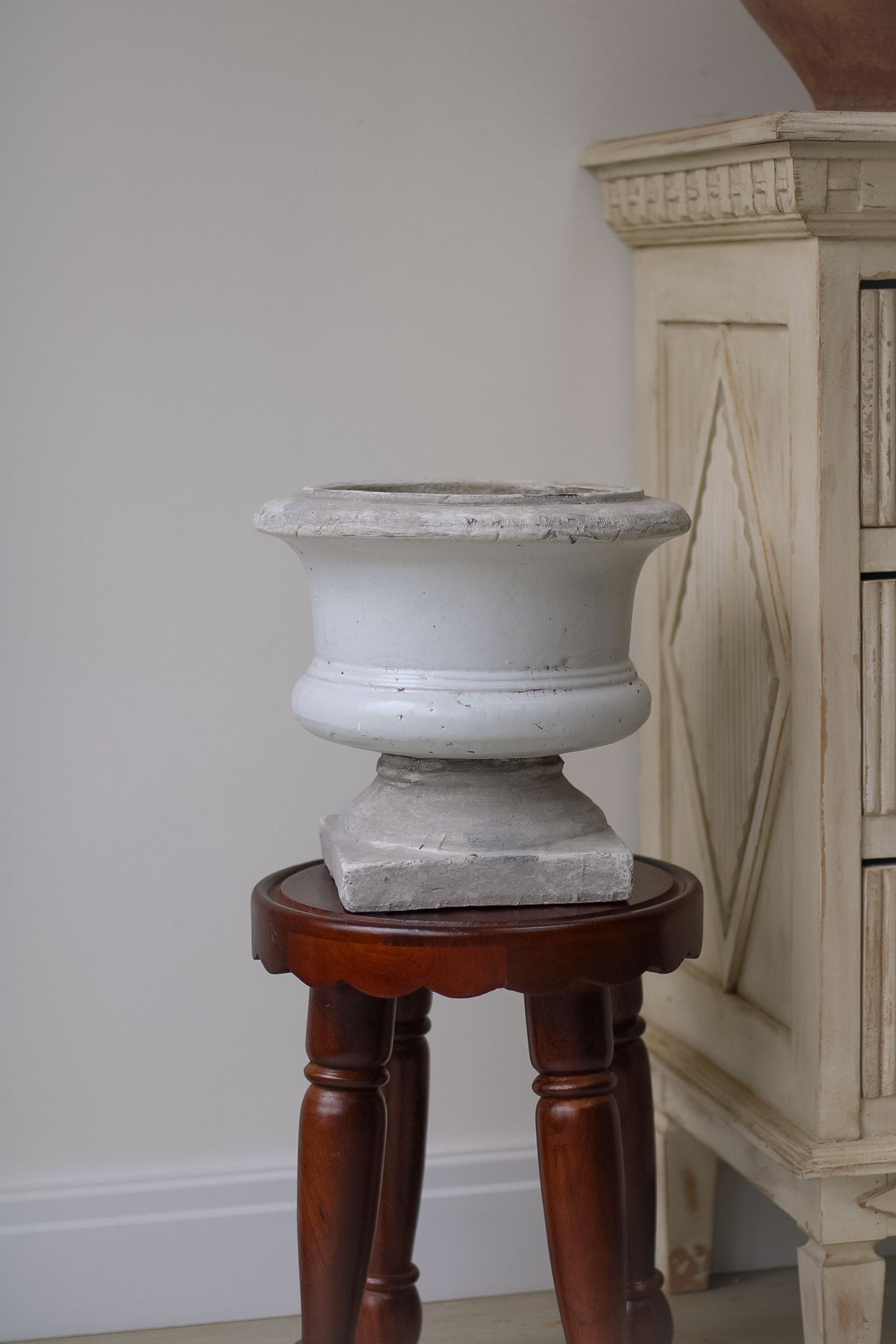 Decorative stone urn on a wooden pedestal against a neutral wall.