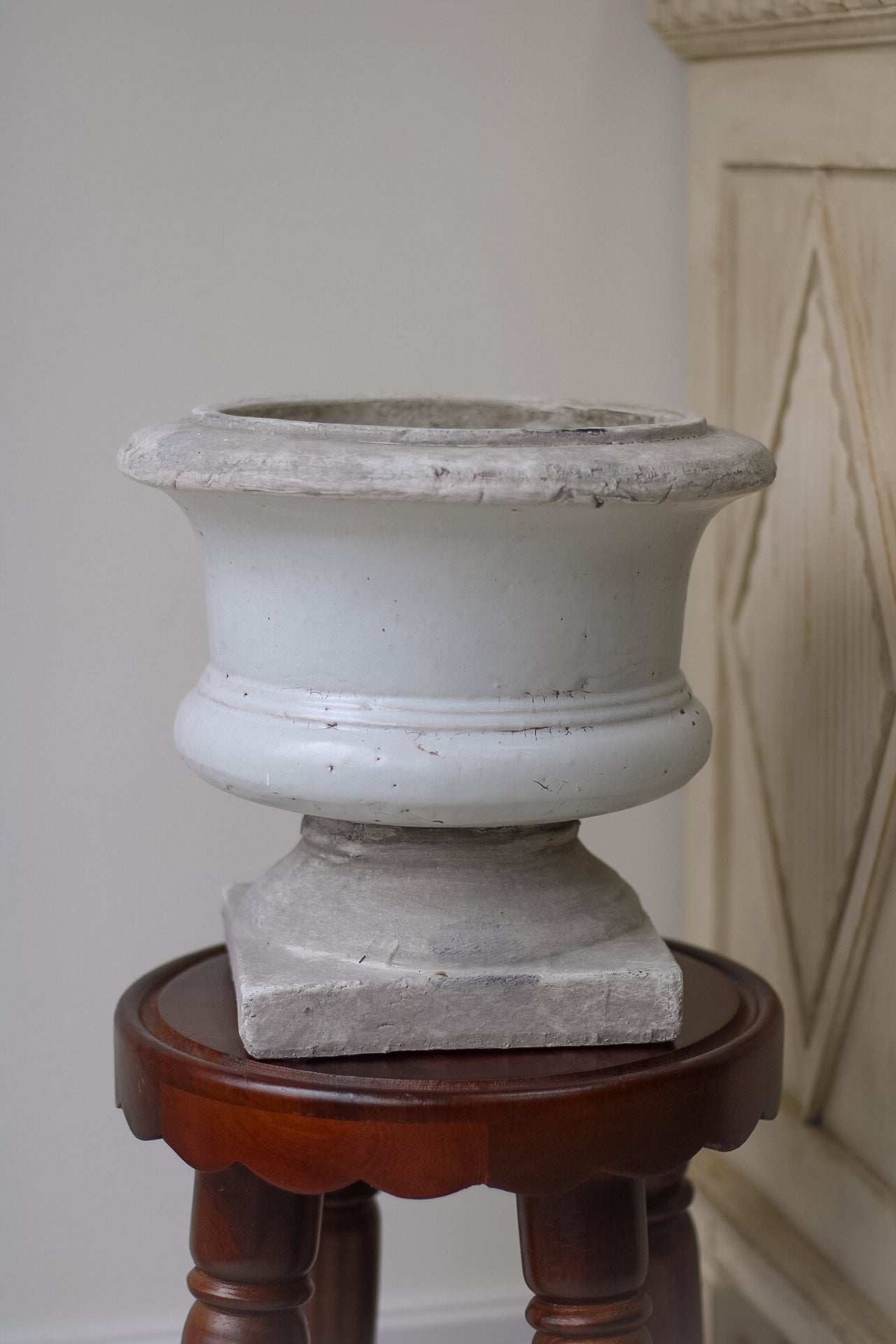 Decorative stone urn on a wooden stand against a plain wall.