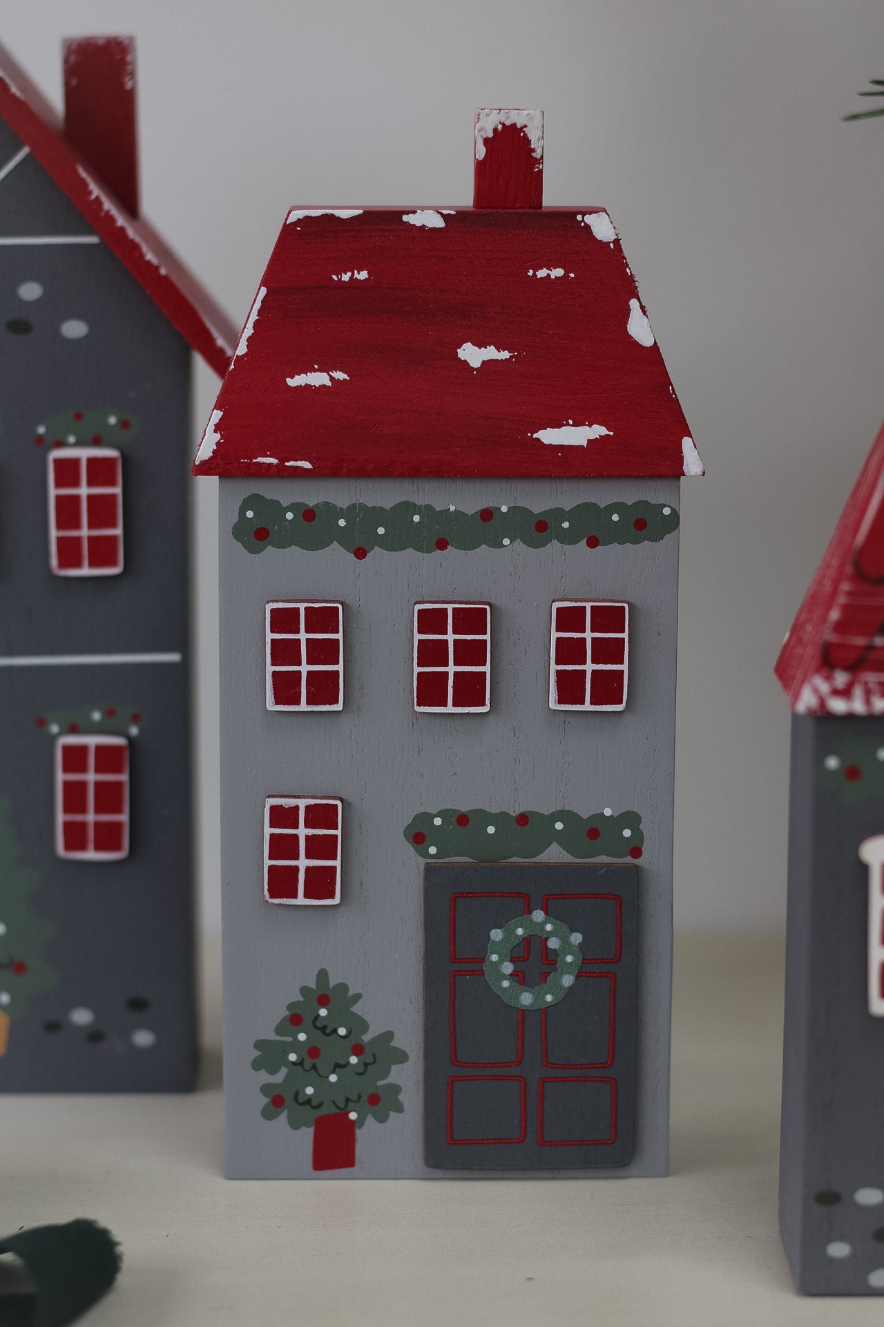 medium light grey wooden christmas house with festive tree, garlands and wreath on the front door